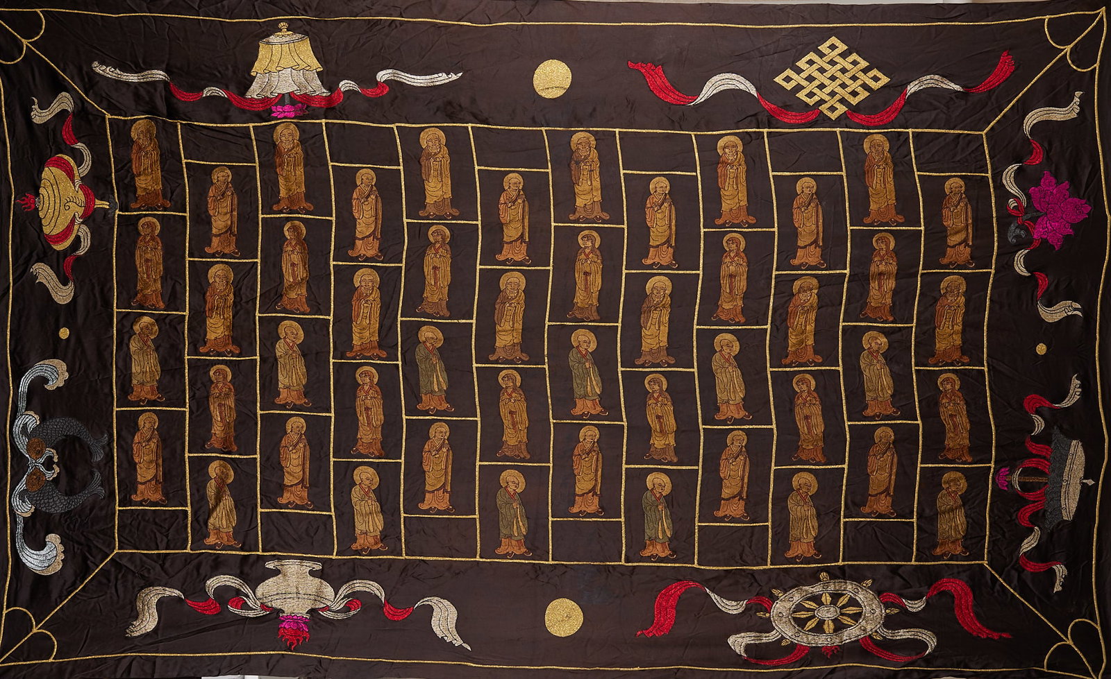 Embroidered arhat warp blanket: Fabric embroidered thangka with dark brown background. Screen grid layout, neatly arranged dozens of arhats, each with a head light. The four corners and sides of the picture are embroidered with