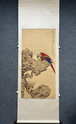 Zhang Daqian's bosom friend map: The paper is colored with vertical axis and framed with silk edge. In the center of the picture, there is a strange Taihu stone, on which two colorful parrots live, and their feathers are red, blue,