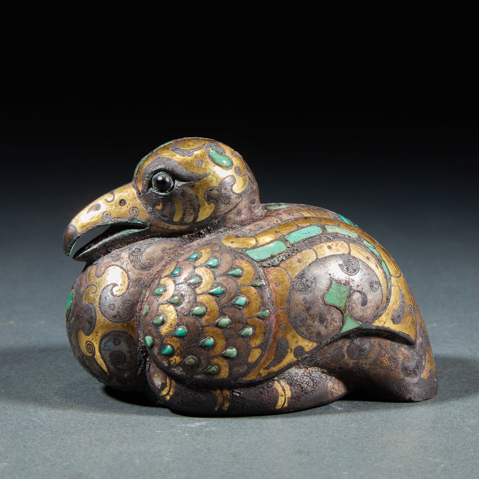 Zhan Han CuO gold and silver inlaid with turquoise God bird-shaped copper town: Bronze texture, recumbent bird curled up and crouched. The body is made of gold and silver, covered with curly patterns, and the bird feathers are inlaid with turquoise. The bird's head is carefully