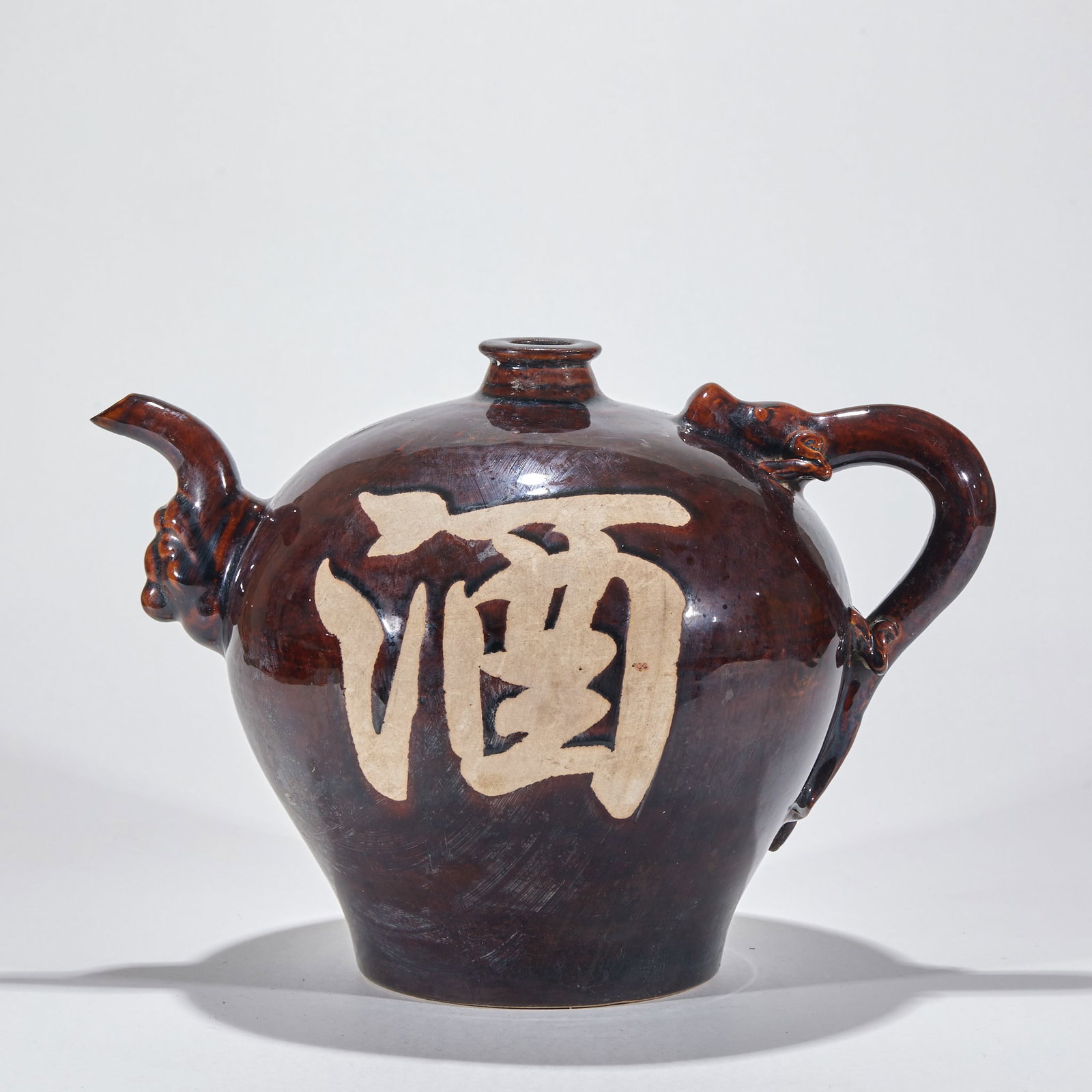Sauce glaze lettering holding pot: Porcelain, with sauce glaze all over. The pot body is round and full, with a small mouth, one side is a beast-shaped spout, and the other side is a plastic beast-shaped handle. On the front of