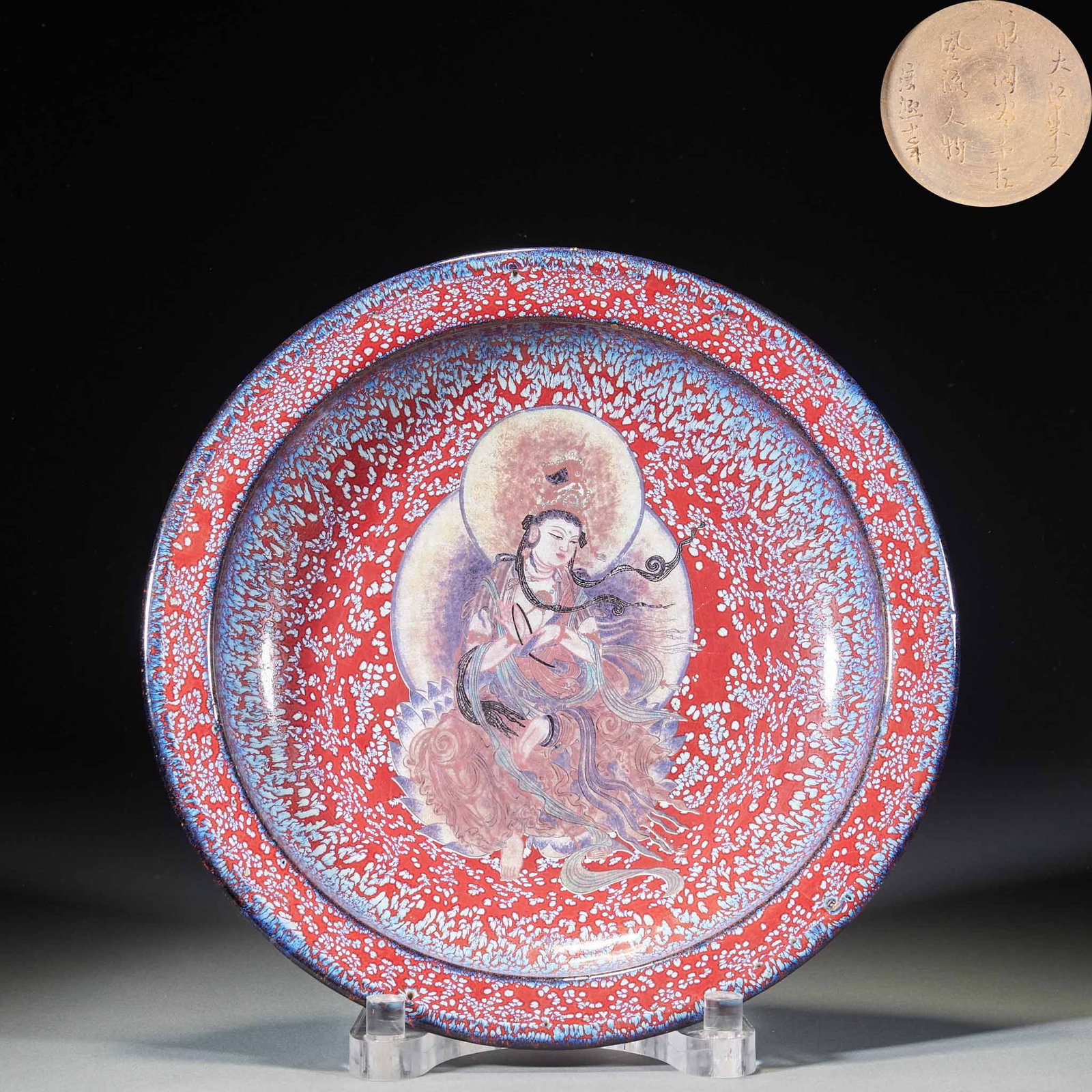 Red glazed Guanyin statue plate: Round folded plate, the opening of the plate is blue and white along the glaze, and the bottom of the plate is red with glaze, covered with fine blue and white kiln spots. A statue of Guanyin is