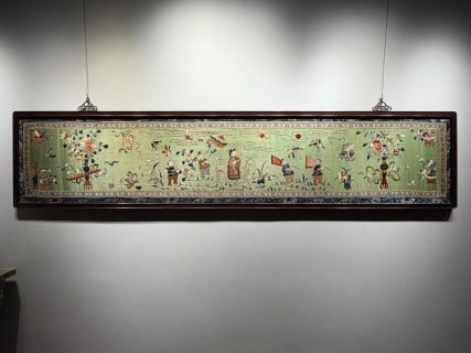 The champion of Suzhou embroidery banner in Qing Dynasty and its: Transverse rectangular embroidery, mounted in a dark wooden frame, hung and displayed with metal hooks. Embroidery is light green fabric, embroidered with multiple groups of figures, flowers, Swiss an