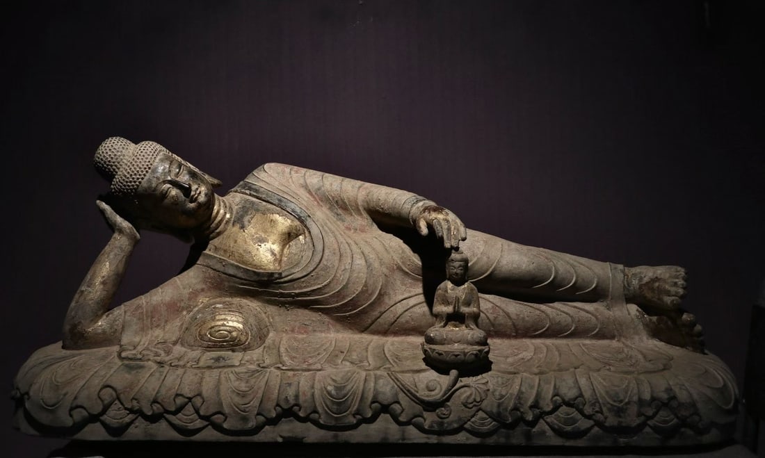 Gold-painted sleeping Buddha statue: The stone nirvana Buddha statue lies on its side, with its right hand resting on its head and its left hand hanging naturally. The Buddha remains gilded and painted, and the folds of the cassock are