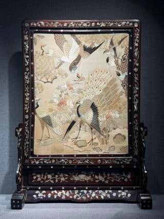Mother-of-Pearl Inlaid Guangdong Embroidery Table Screen, Late Qing-Republic: With a rosewood frame inlaid overall with mother-of-pearl flowers and plants. The screen centre is embroidered with a peacock, cranes, a hundred birds and peonies: the peacock fans its tail amid full