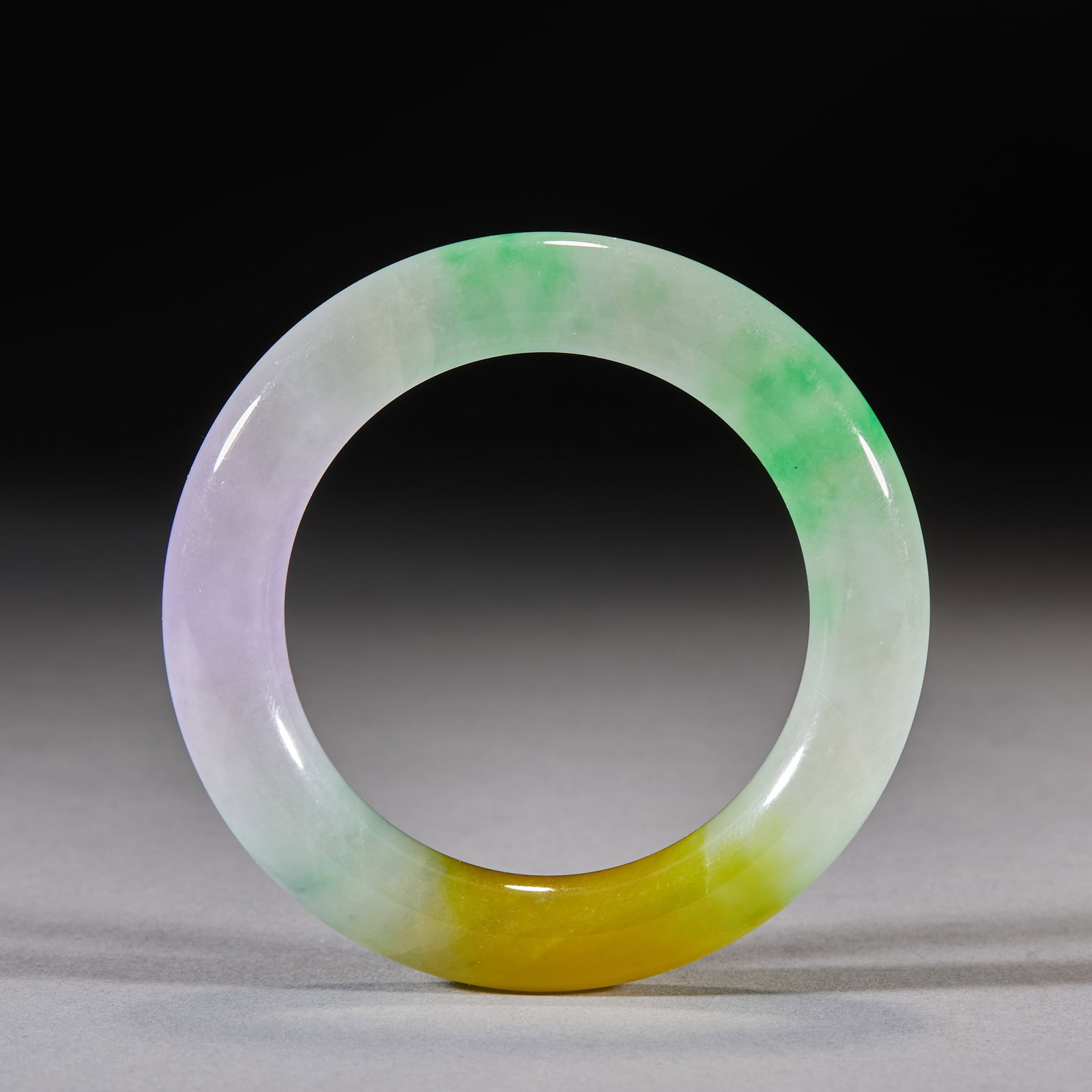Jadeite Bangles: Round-section bangles showing green, purple and yellow in one piece, of translucent stone with a lustrous polished surface. Inner diameter 5 cm.