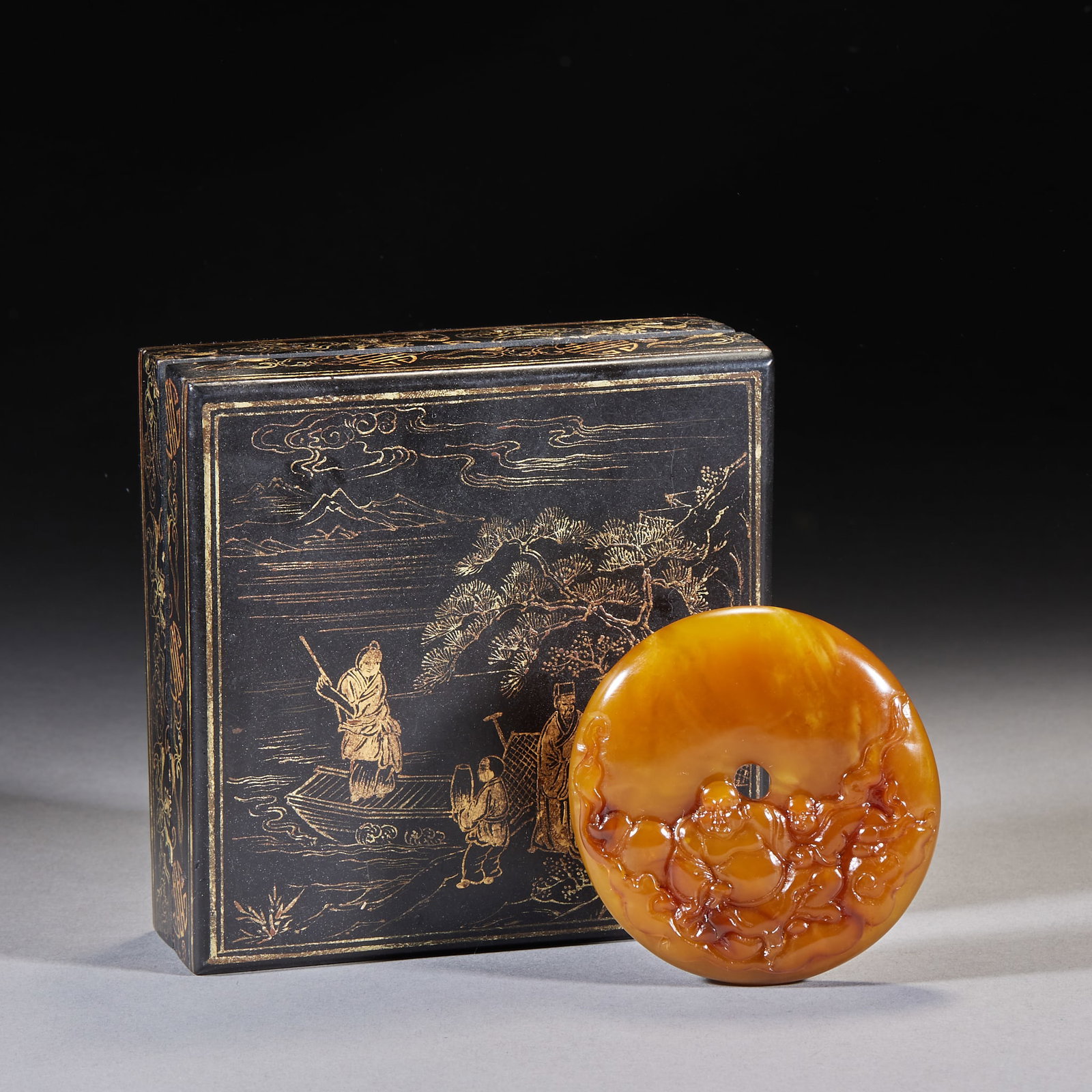 Tianhuang Stone Bi Carved with Sutra on Back, Maitreya Offering Treasure: A circular bi; the outer face is carved in relief with Maitreya and a boy. Supplied with a square black-lacquered box whose lid is gold-traced with a landscape-figure scene. H 1.1 cm, Diameter 7.5