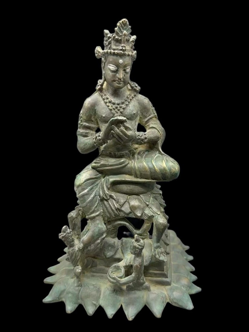Copper Swat Seated Buddha: Of bronze with old patina. The Buddha wears a crown and multiple strands of jewelry, seated in full lotus position on a lotus throne with a small guardian figure below the base. H 23 cm.
