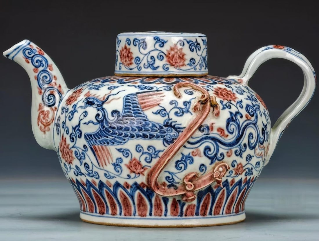 Xuande-Marked Underglaze-Blue and Copper-Red Ewer with Dragon-Phoenix and Floral Scrolls, Ming: Of white porcelain; the body is painted with a phoenix in underglaze blue and copper-red floral scrolls, with an applied iron-red chi-dragon. Cover, spout and handle complete; lotus-petal band near