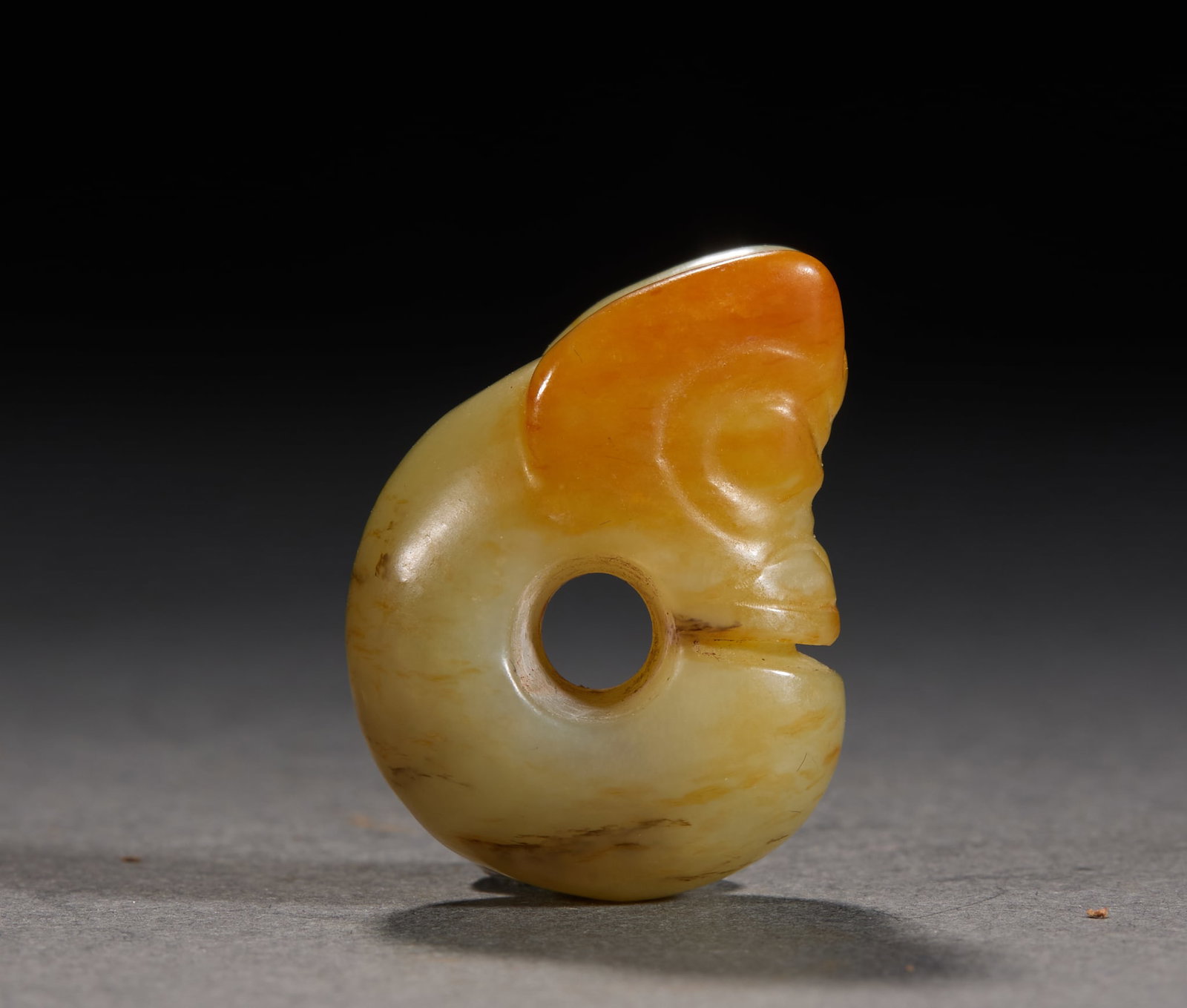 Hongshan Jade Pig-Dragon: A classic Hongshan-culture pig-dragon. Of yellow jade with patches of orange-red skin; C-shaped and coiled, the beast head has round large ears and eyes, a protruding snout, a hole through the