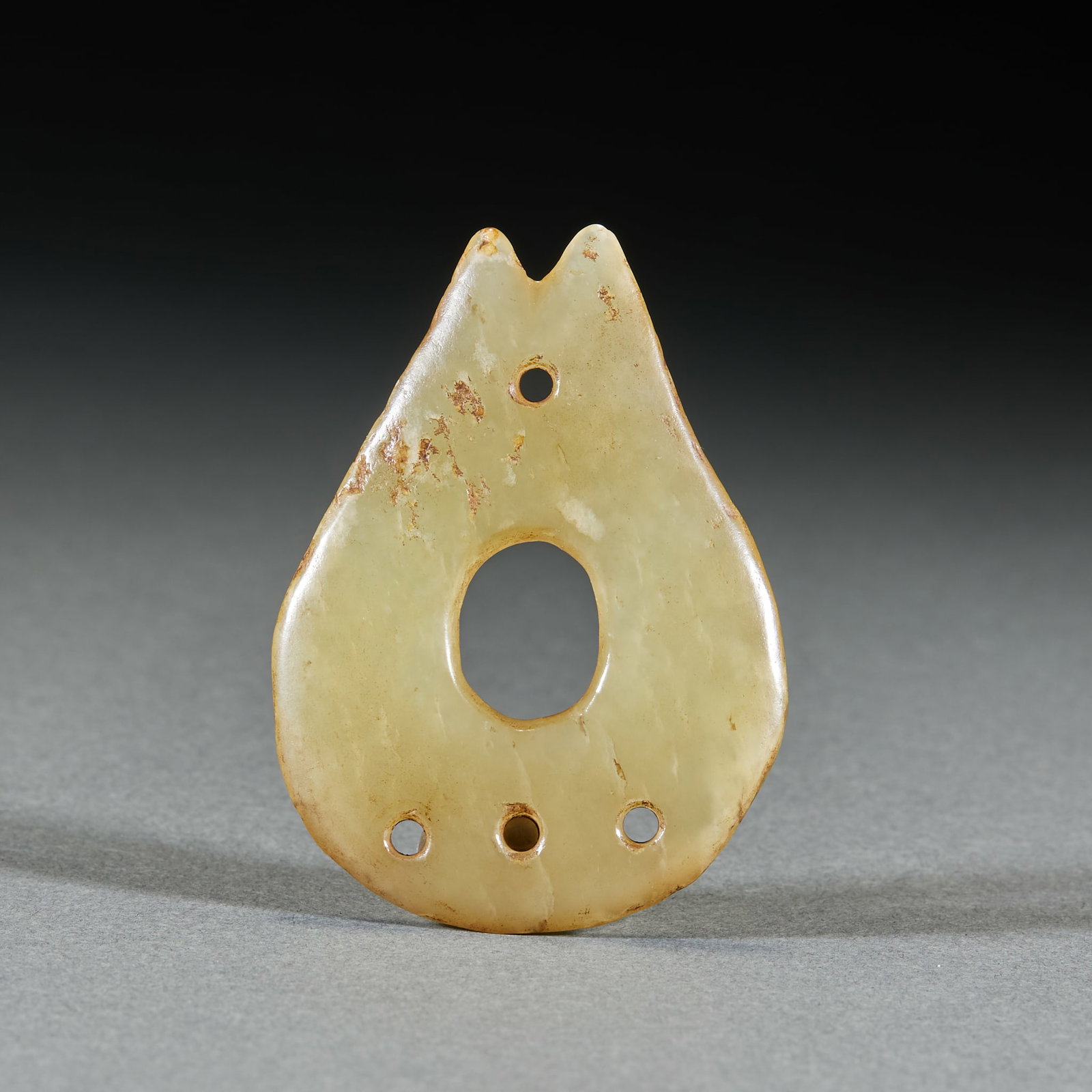 Hongshan Lingbi Pendant: Of greenish-yellow jade shaped like a water-drop heart with two pointed ends above, a large central hole, four small holes on the body and ancient earth-calcification at the edges. A prototype of the