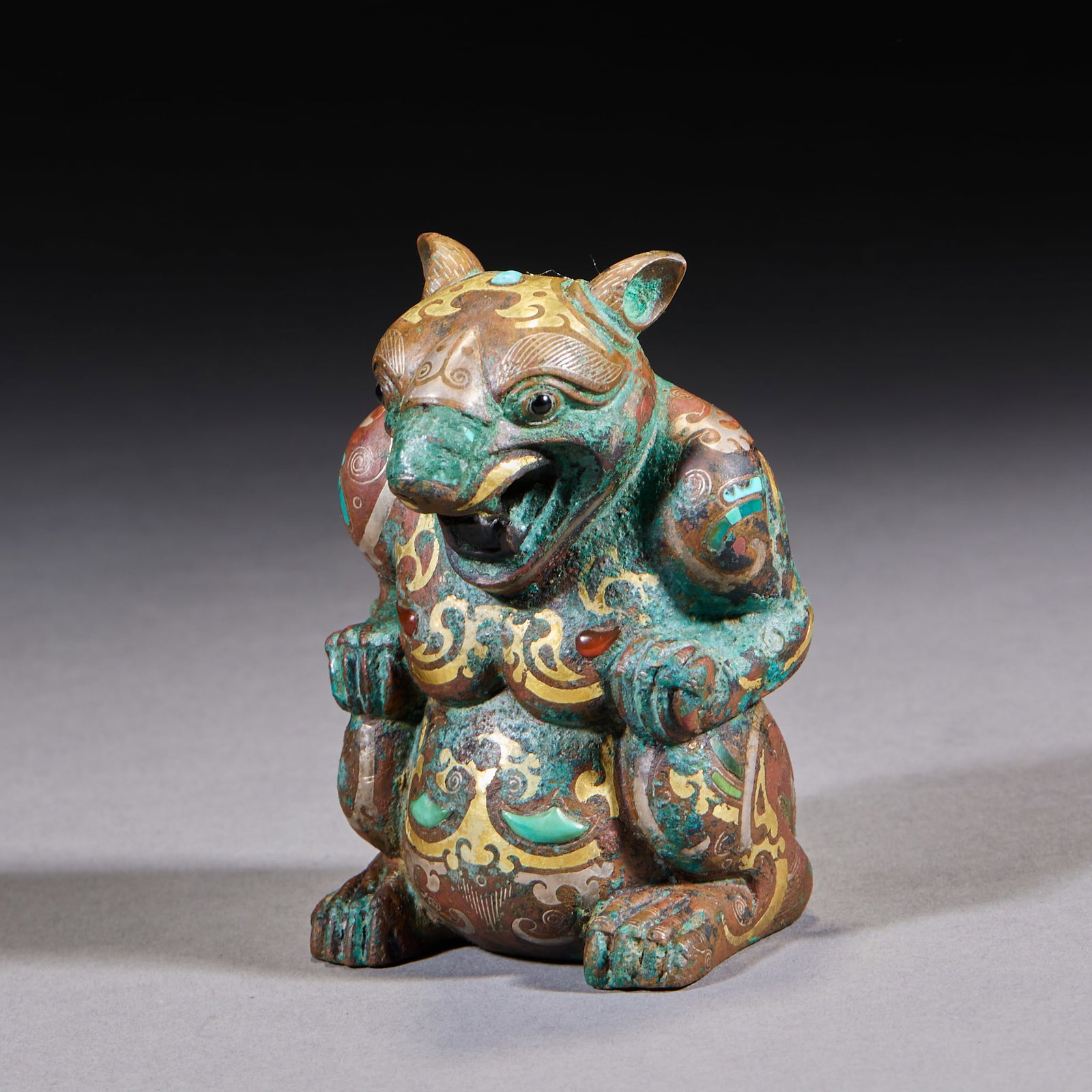 Inlaid-Gold-and-Silver Jewel-Inlaid Bear Warrior: A crouching bronze bear inlaid with gold and silver and set with turquoise and red agate. The bear sits, mouth open showing teeth, muscles full and body covered with cloud-scroll patterns. A