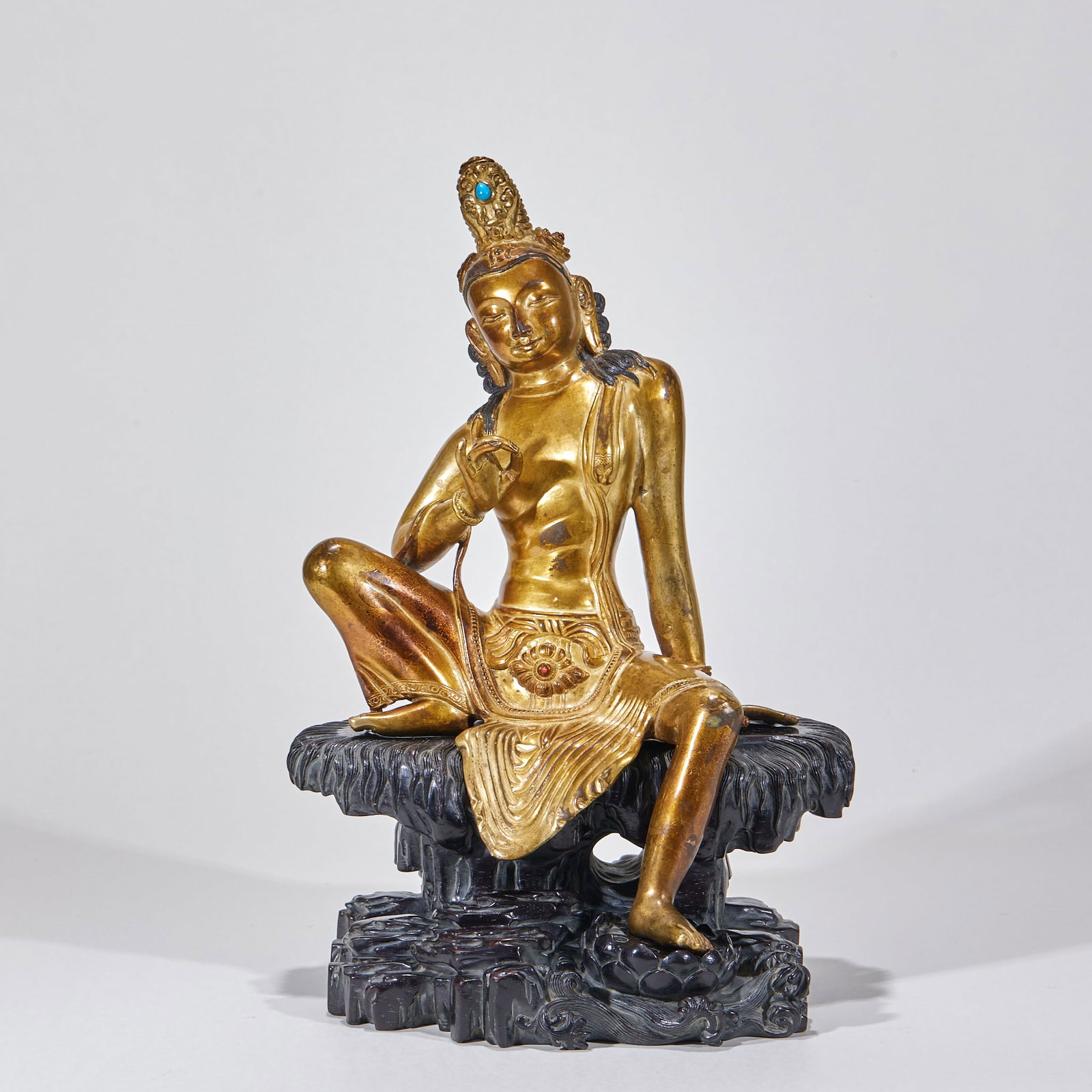 Gilt Copper Buddha Figure on Zitan Stand: A gilt-copper Laughing/Water-Moon Guanyin seated in a relaxed half-lotus pose on a wooden mountain-rock stand. She wears a crown set with turquoise; the jewelry and sash are fluidly carved and the