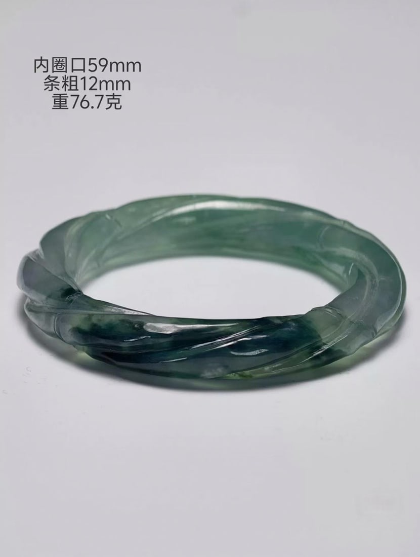 Jadeite Twisted-Cord (Ma Hua) Bangle: A natural jadeite twisted-cord bangle, inner diameter 59 mm, bar 12 mm thick, weight 76.7 g. Of high-ice stone, translucent with a sheen and blue-green colour float, made by the cord-twisting carving