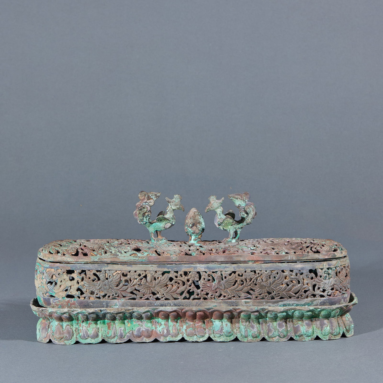 Copper Phoenix-Head Incense Burner: An oblong openwork incense burner; the cover is topped with twin phoenixes and a jewel finial; the body is pierced throughout with phoenix-and-floral-scroll patterns, over an upturned-lotus base. A