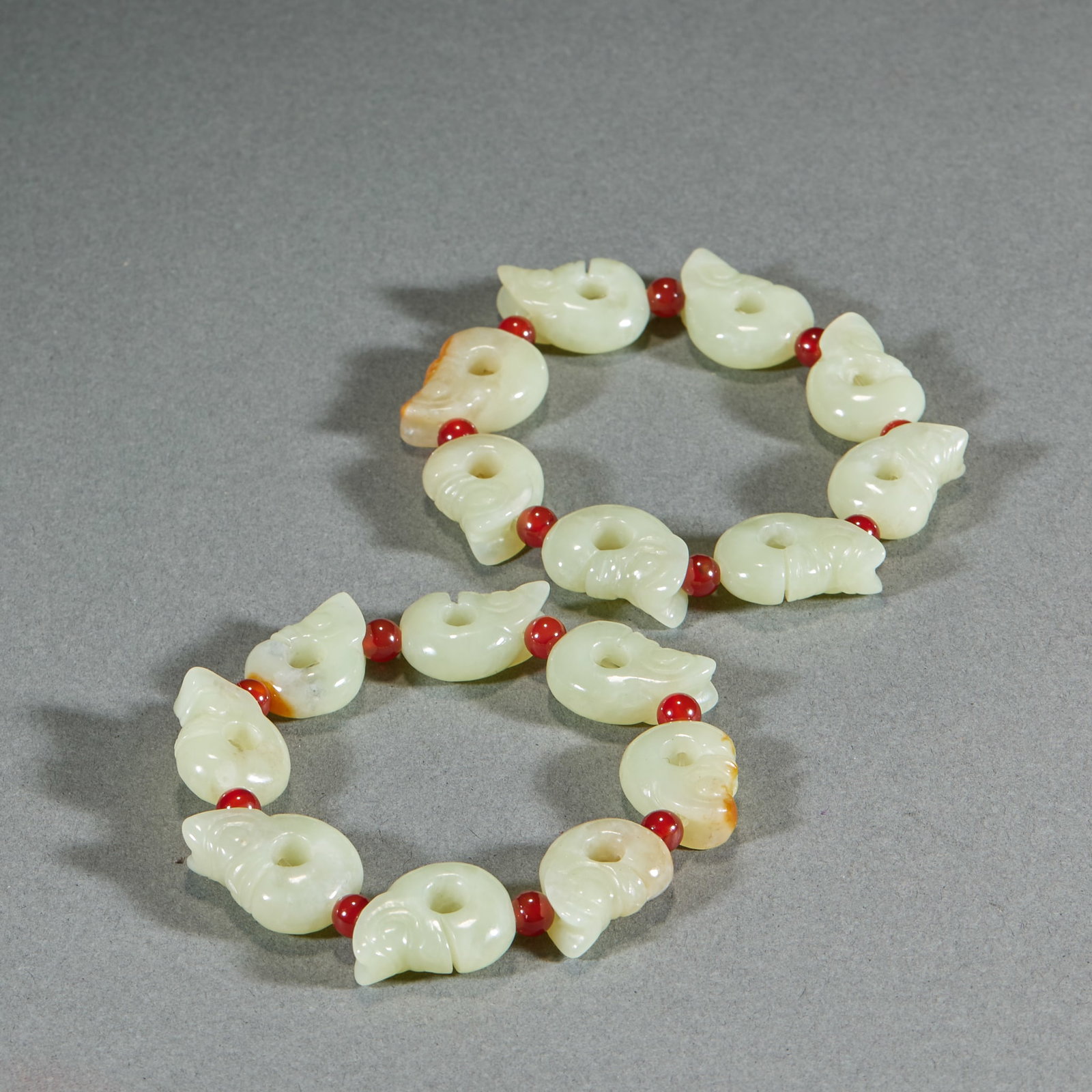 Pair of Jade Pig-Dragon Bracelets: Strung of several jade pig-dragons with red agate spacers. The jade is greenish-white with natural yellow-brown calcification; the coiled forms have notched mouths ?? classic archaic beast-form jade