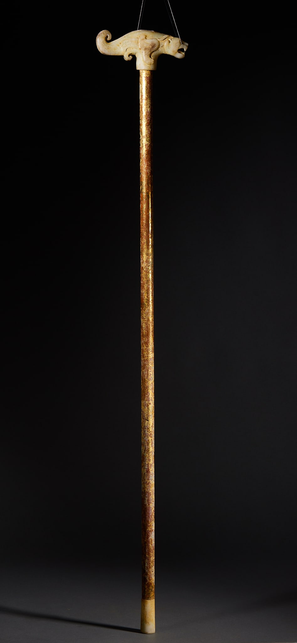 Pre-Ming Chi-Tiger-Head Walking Stick: The ferrule is a white-jade carved tiger head with lively curling lines; the shaft is gilded throughout and fitted with a jade tip. Complete in form ?? a traditional ceremonial walking stick. L 88