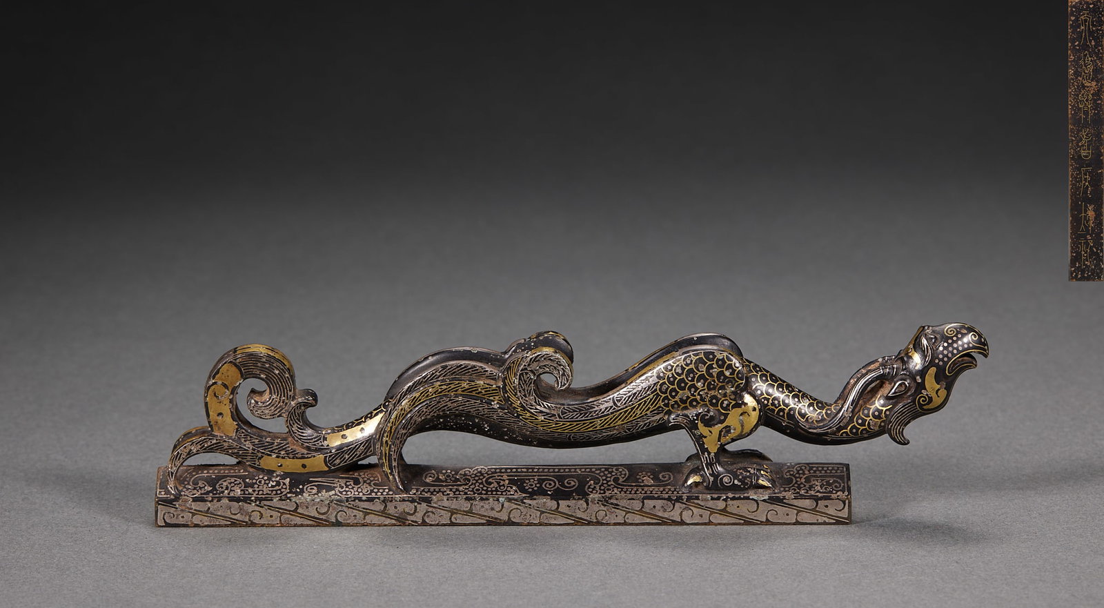 Pre-Ming Inlaid-Gold-and-Silver Phoenix Paperweight: An old bronze inlaid gold-and-silver (cuo-jin, cuo-yin) scholar's paperweight. The phoenix is coiled with the body inlaid in gold and silver wire with scale and cloud patterns ?? an elaborate craft