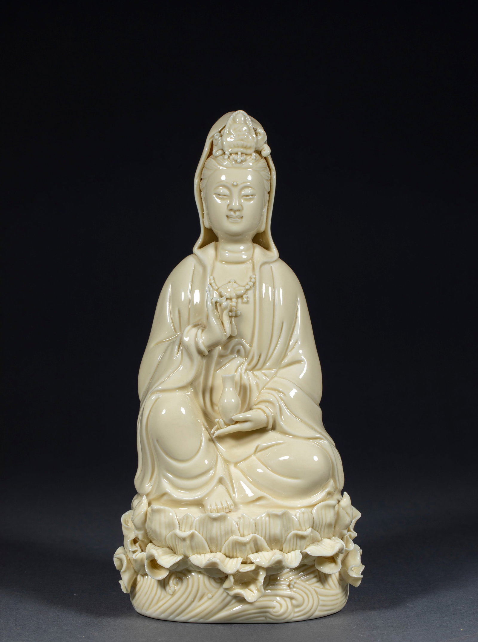 Dehua Kiln He Chaozong Seated Guanyin: Dehua ivory-white porcelain: the Guanyin sits in lotus position on a lotus-and-wave base holding a pure-vase, with a gentle face. Dehua white ware is known as 'lard white'; the Ming-Qing Dehua