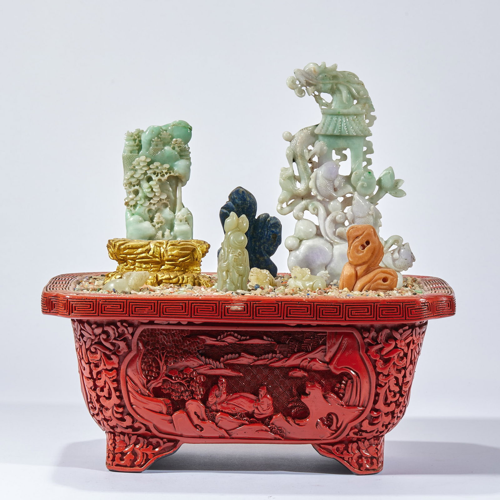 Lacquer Hetian Jade Bonsai: A red carved-cinnabar-lacquer flower pot carved with a landscape-figure scene; within is a multi-treasure display of jadeite, lapis lazuli, Shoushan stone and other gems carved as mountains, beasts,