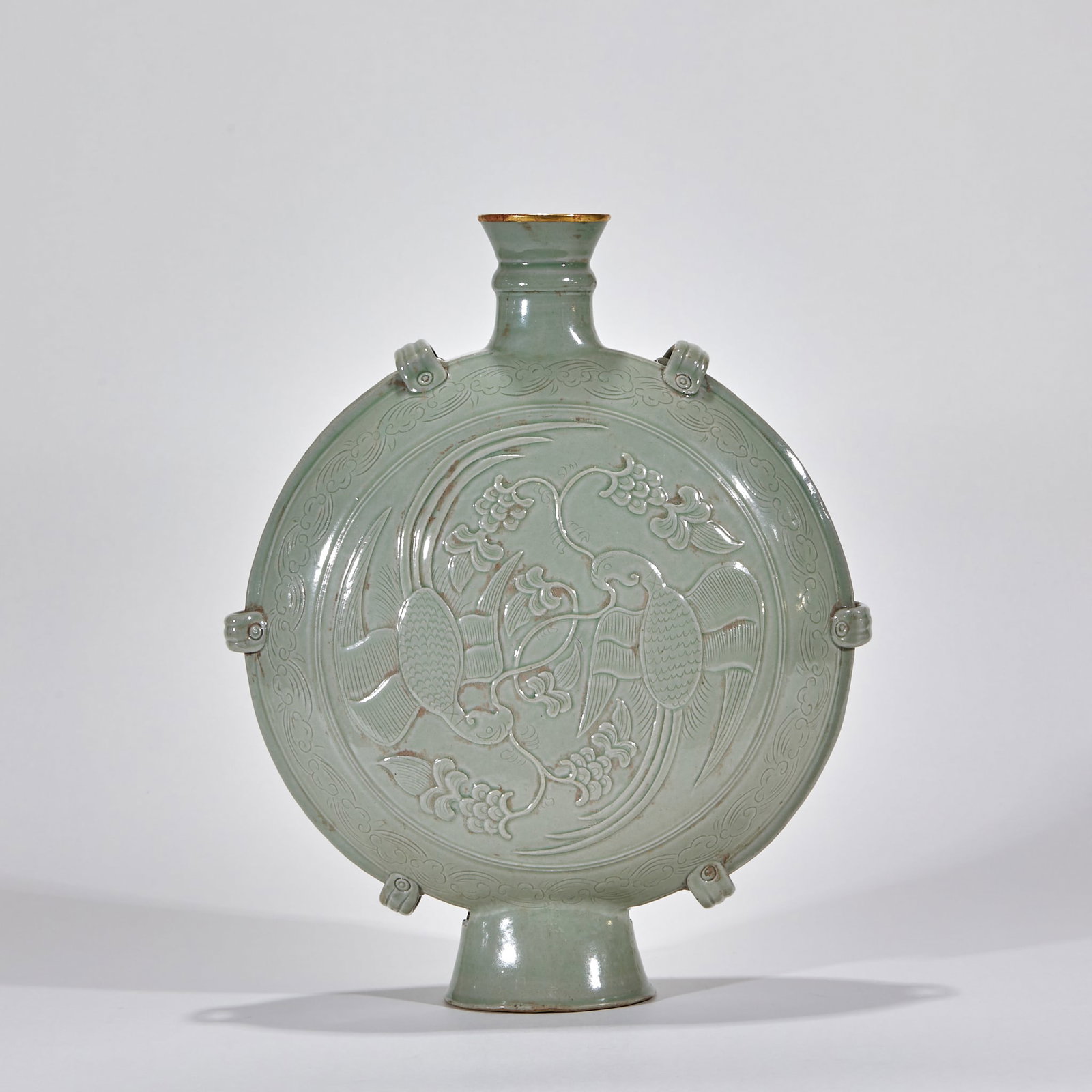 Yue Kiln Gold-Rimmed Phoenix Moon-Flask: Glazed overall in powder-green celadon; the flat rounded body is carved with a pair of ribboned phoenixes amid grapes and flowers, ringed by eight loop ears, the mouth wrapped in gold. Longquan is a