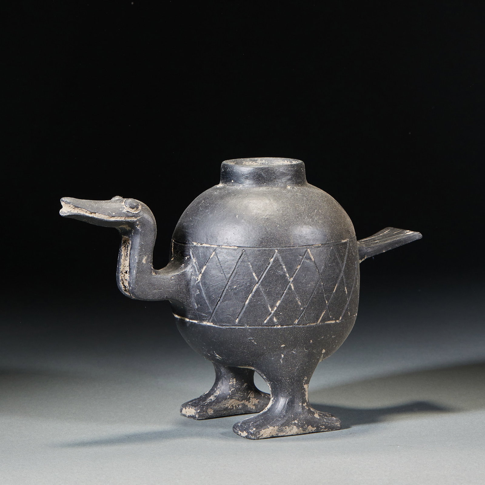 Black-Pottery Crane-Form Vessel: A black-pottery duck/crane shape with the duck head as spout, tail as handle, supported on two duck feet. The body is incised with geometric diamond patterns. Prehistoric or pre-Qin ancient pottery, z