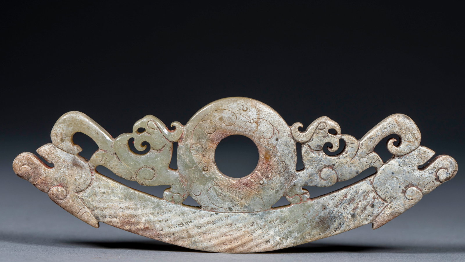 Twin-Dragon Jade Huang (Arc Pendant): Ancient jade, clearly calcified. The principal is a jade huang arc linked to a central bi disc, with dragon heads at both ends and a chi-dragon carved beside each side of the disc. A high-ranking