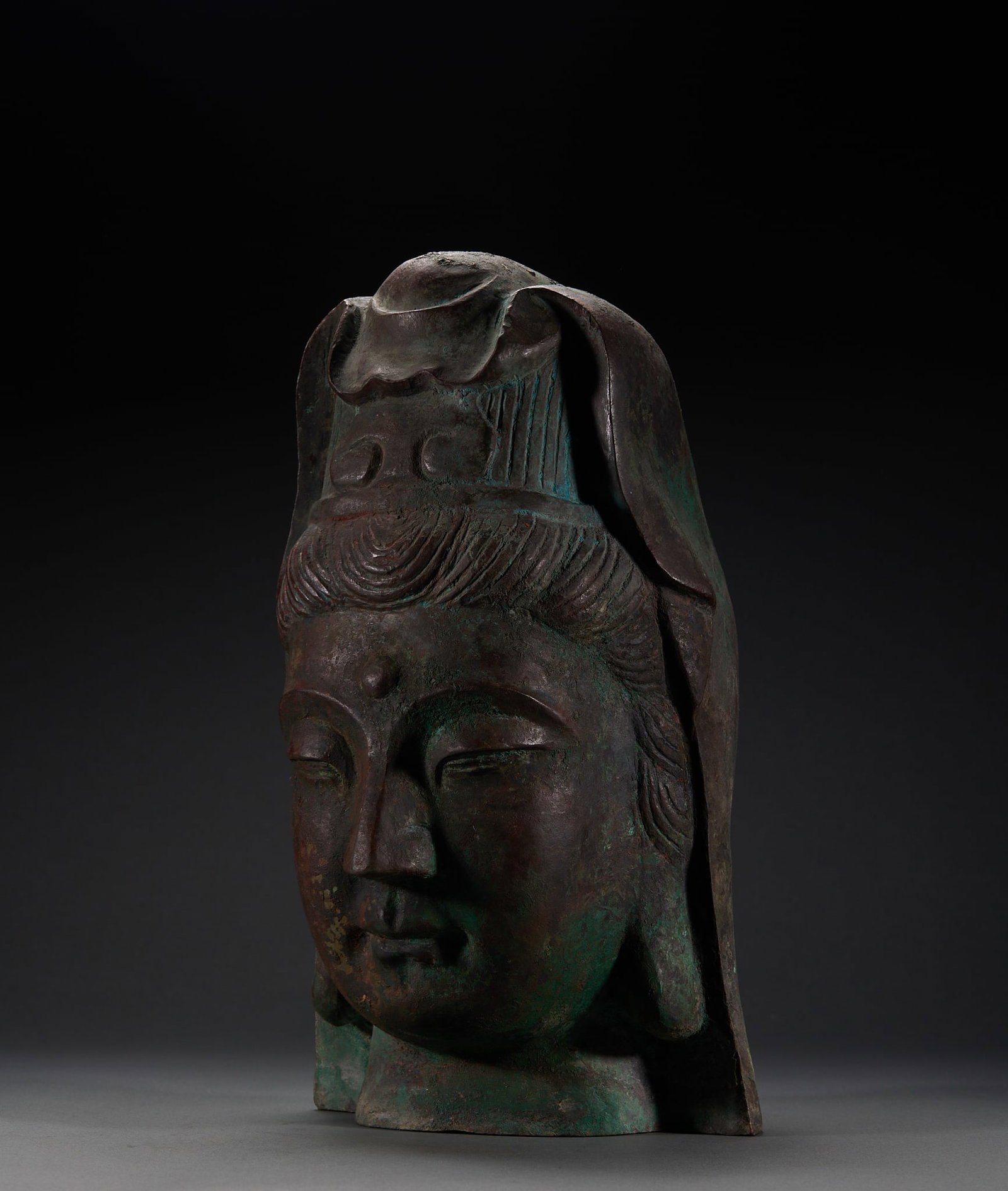 Copper Head of Guanyin: A bronze cast head of Guanyin with a tall crown, finely rendered hair, and a calm, compassionate face. Covered with blue-green patina, archaic and dignified, richly sculptural. H 31.5 cm, L 17.5 cm,