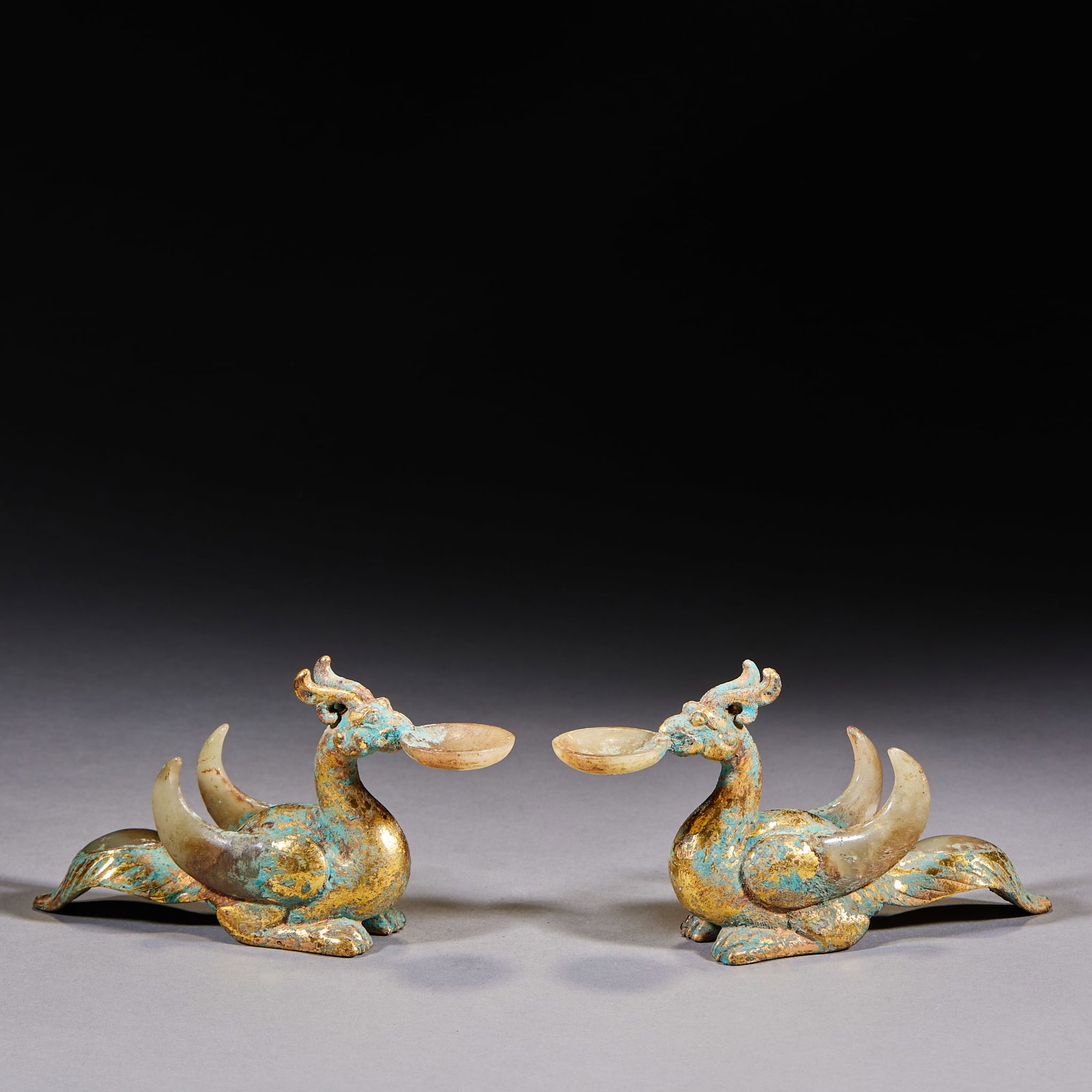 Gold-Inlaid Jade-Inset Beast-Ear Ring-Handled Square Vessel: Gilt-copper, cast as a phoenix-bird form: the phoenix head holds a shallow jade cup in its mouth, and two jade huang-arc ornaments are set into the tail; the body bears verdigris and traces of gilding