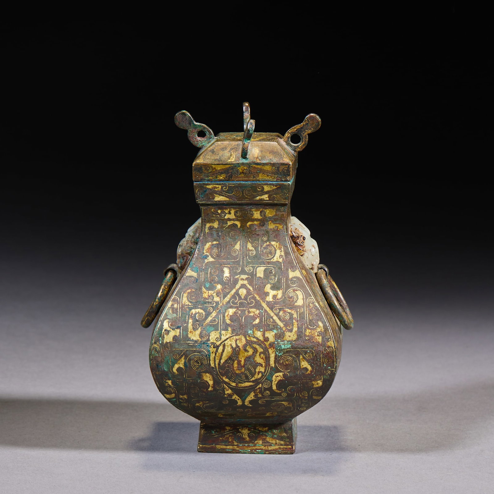 Jade-Inset Four-Footed Three-Dragon-Head Bear-Supporting-Heaven Lamp: A Han-style bronze ritual vessel. The body is a square flat-flask form with square cover and ring knob; inlaid throughout with gold in complex meander and phoenix patterns, with movable-ring beast