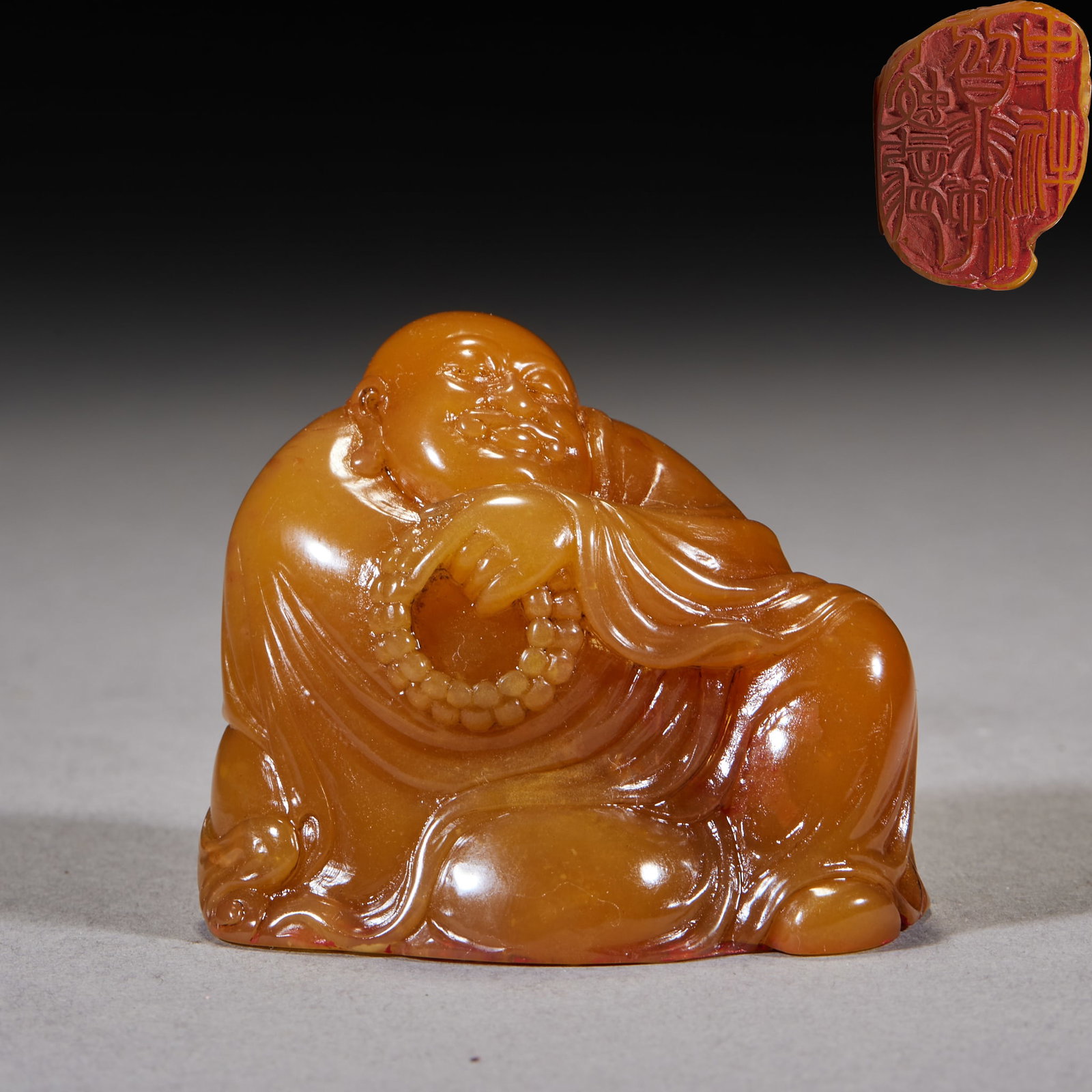 Tianhuang Stone Seated Arhat Holding Beads with Seal: A Shoushan tianhuang round carving of a seated Maitreya holding prayer beads with a full smile, the stone warm honey-yellow. The base is cut with a red (yang) seal inscription ?? usable both as a scho
