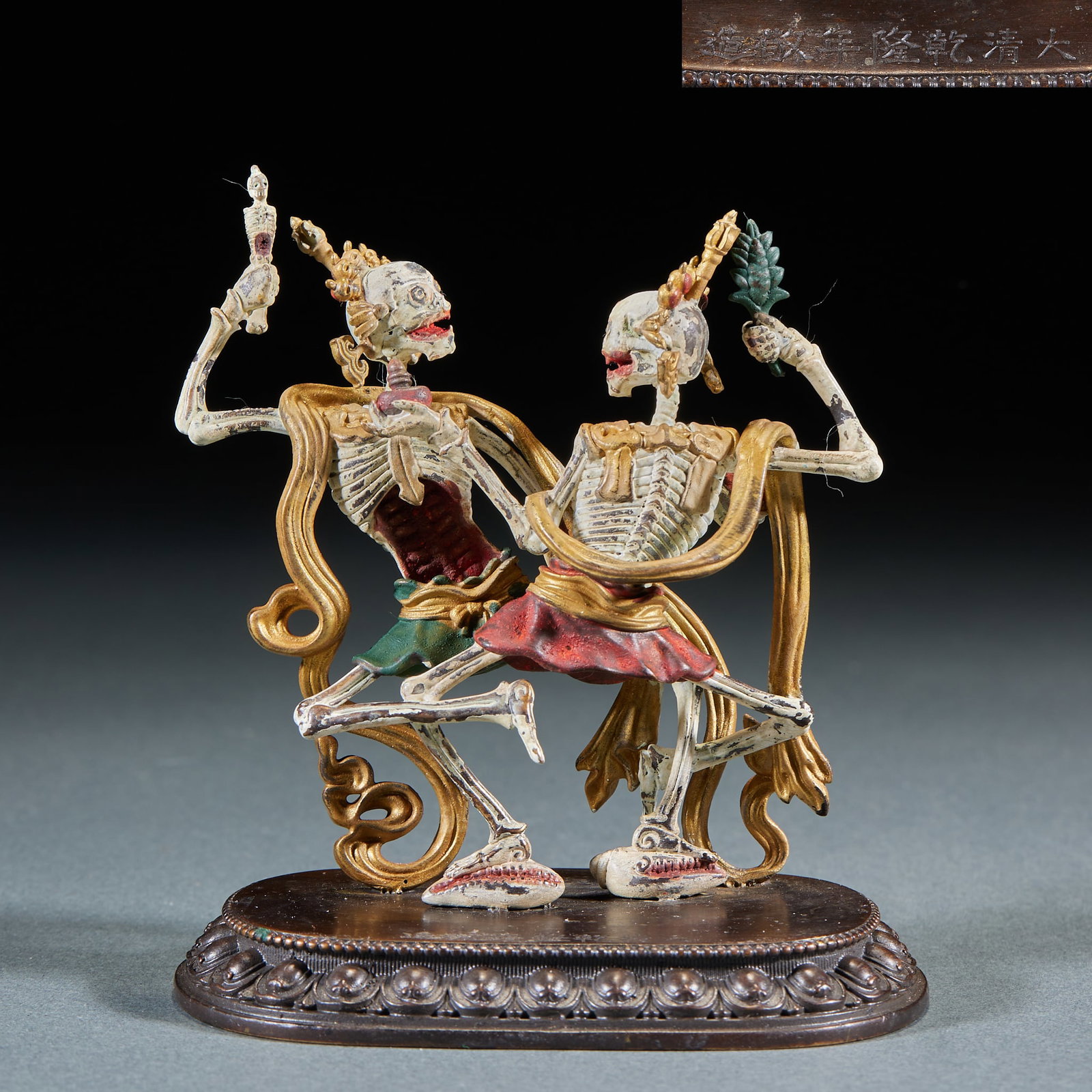 Gilt Copper Citipati Dual-Figure, 'Made with Reverence in the Qianlong Reign of the Great Qing': Copper-bodied painted: two skeletal divinities embrace in dance, garments gilded and painted, the base inscribed 'Made with reverence in the Qianlong reign of the Great Qing'. The Citipati are