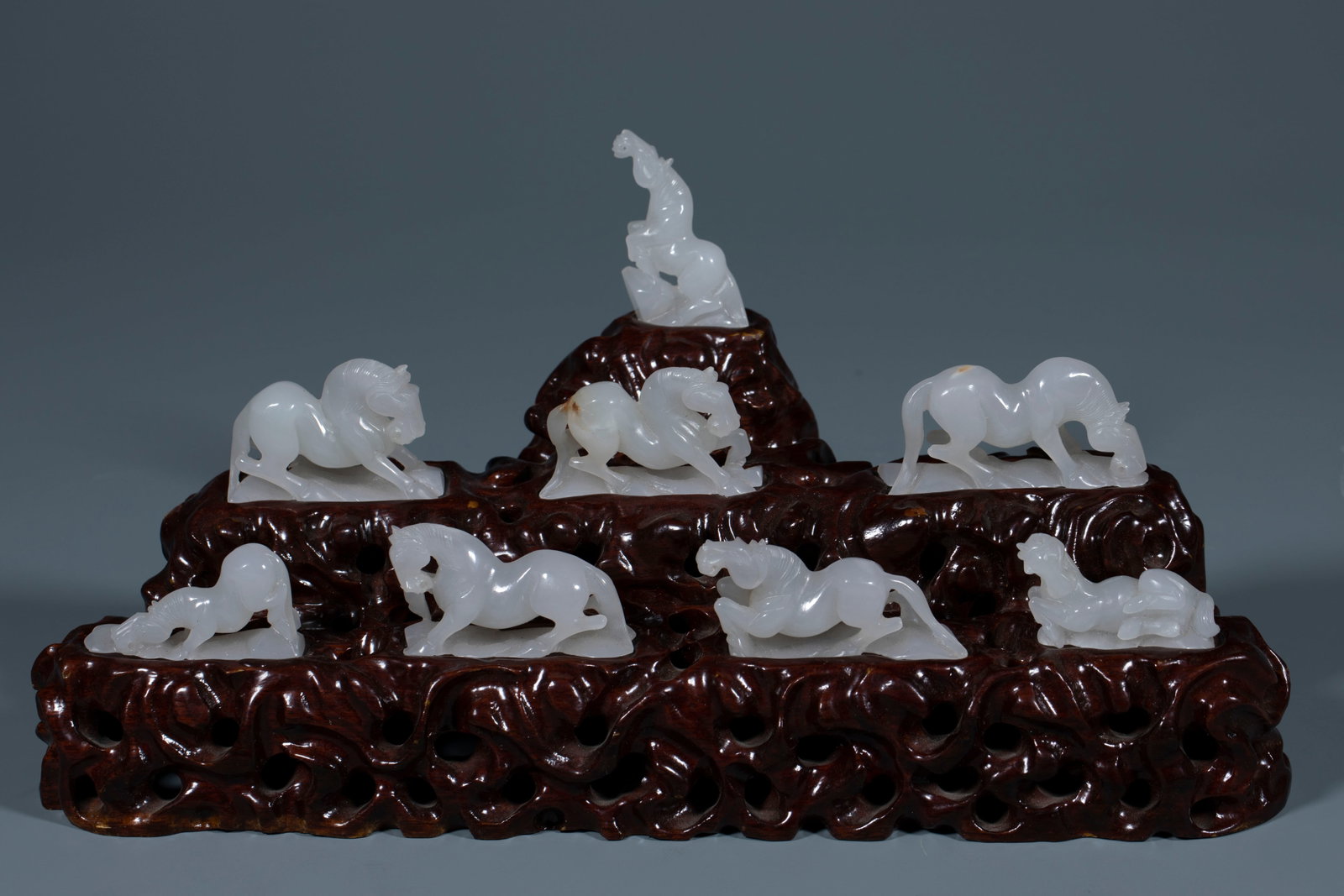 Qing Hetian Jade Eight Steeds Ornament: A complete set of eight white Hetian jade horses in varied poses ?? standing, reclining, galloping, drinking, looking back ?? of white, lustrous, fine jade, on a single natural-form rosewood base.