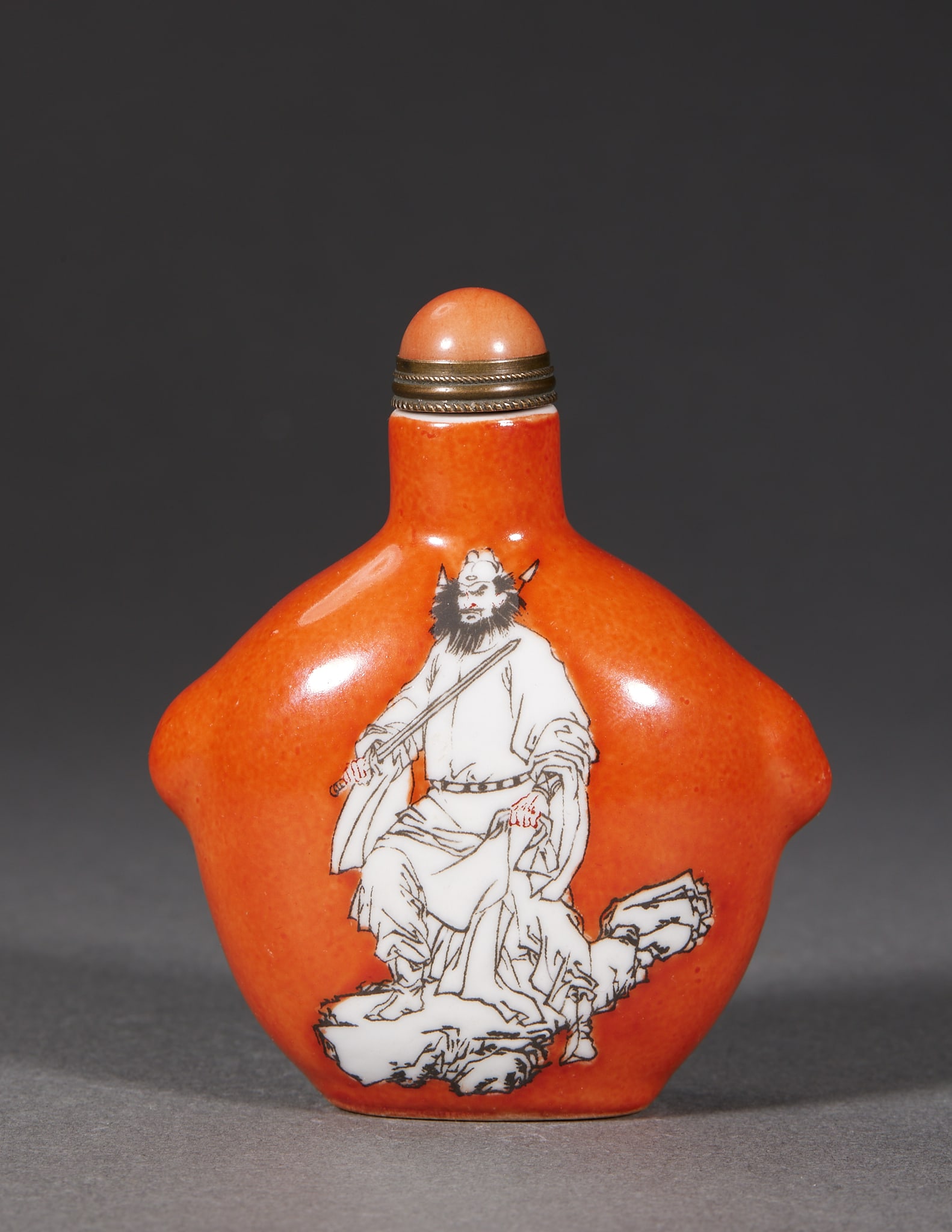 Qing Zhong Kui Snuff Bottle: An iron-red-ground porcelain snuff bottle with flanged ridges at the sides; on the iron-red ground a sword-holding Zhong Kui is painted in ink-colour and white, standing on rocks with a stern expressi