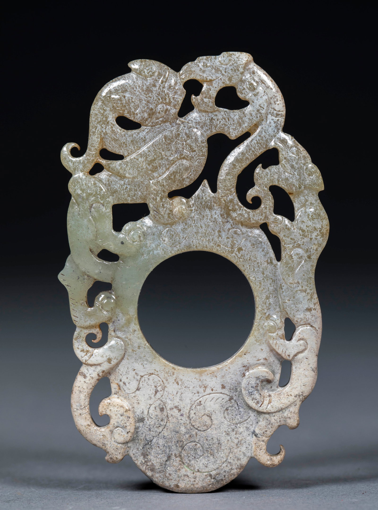 Openwork Chi-Dragon-Fighting-Tiger Heart Pendant: Of greenish-white jade in she-pendant form, the surface covered with grey-white calcification. Cut in openwork: dragons and phoenixes intertwine above, chi-dragons and phoenixes wheeling ?? archaic