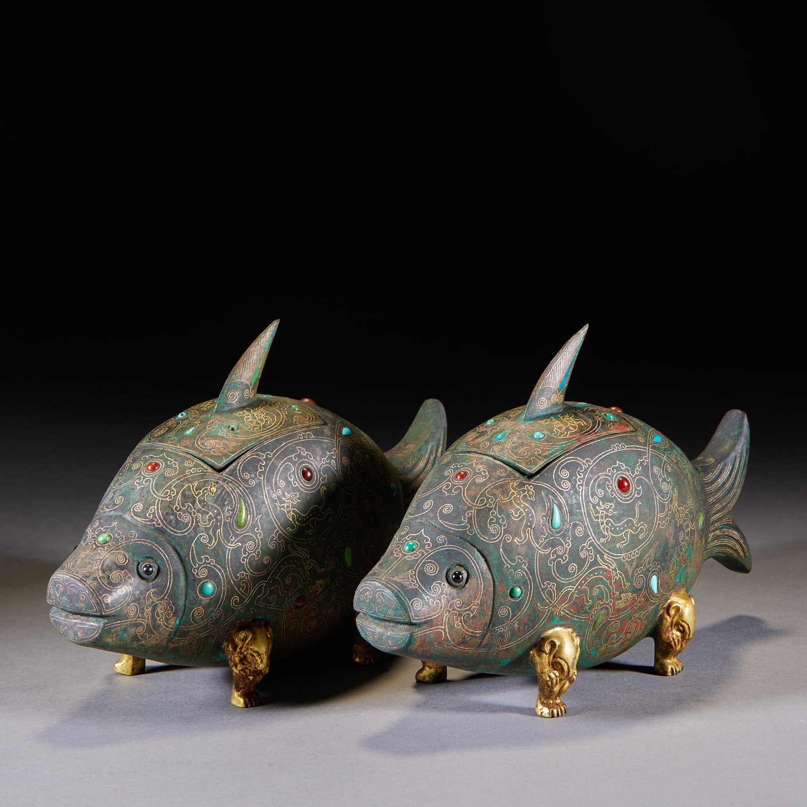 Pair of Inlaid-Gold-and-Silver 'Hundred Longevity' Fish-Form Covered Jars: A pair of fish-form bronze zun: the fish bodies are inlaid in gold and silver outlining cloud-dragon motifs and set throughout with multi-coloured gems. Gilt beast feet support the fish; the fish