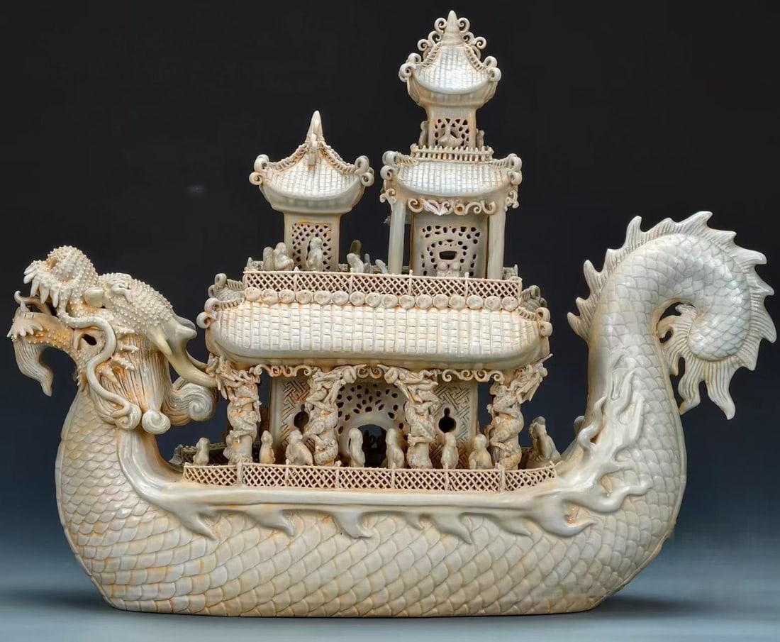 Hutian Kiln 'Smooth Sailing' Porcelain Dragon Boat: A greenish-white glazed porcelain dragon boat of large scale, modelled overall as a dragon head and tail. The hull carries multiple tiers of pavilions with great amounts of pierced railings and