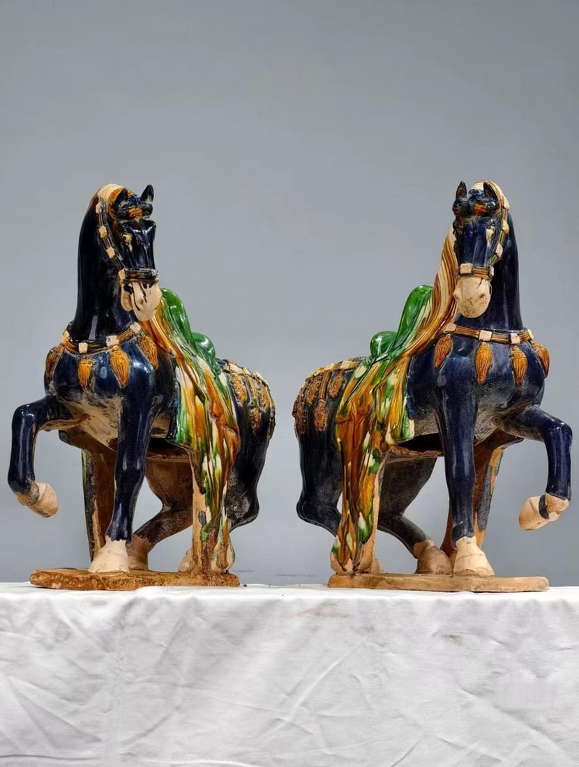 Pair of Sancai Steed Figurines: A pair of Tang sancai (three-colour) standing horses, the bodies chiefly deep-blue glaze with green and yellow saddlery. The horses raise a hoof and lift the head, manes falling; the glaze flows natur