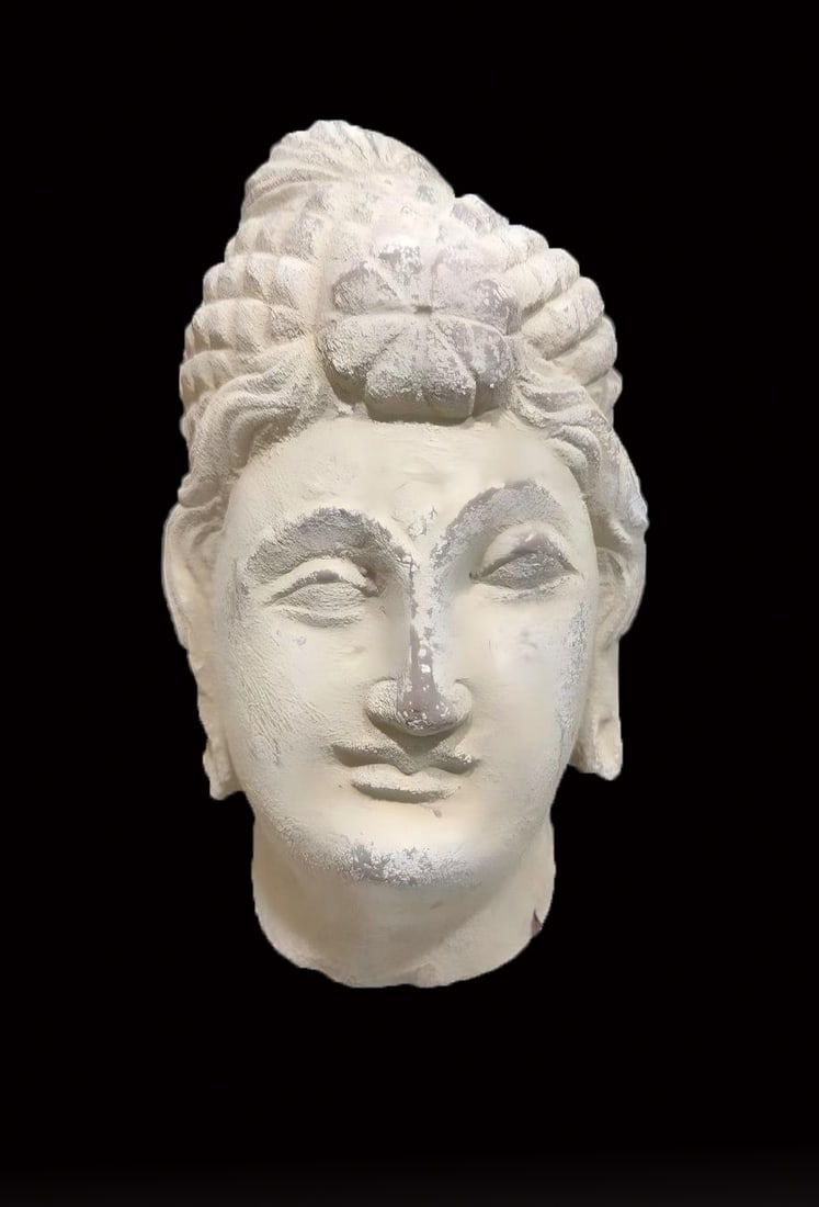 Gandhara Head: A stone bodhisattva head with a high bun adorned with flowers, curling hair, a soft face and lowered eyelids, a serene air; it carries a foreign sculptural style, with natural weathering. (no