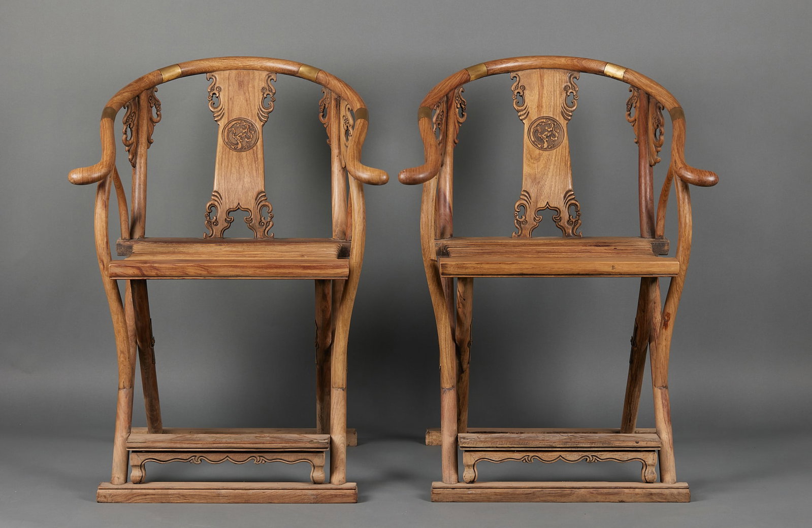 Pair of Huanghuali Phoenix-Back Folding Chairs: A pair of Huanghuali folding chairs with curved backrests carved in relief with phoenixes, wings spread and tails splendid. The seats are woven rattan soft panels, folding for storage. The wood is