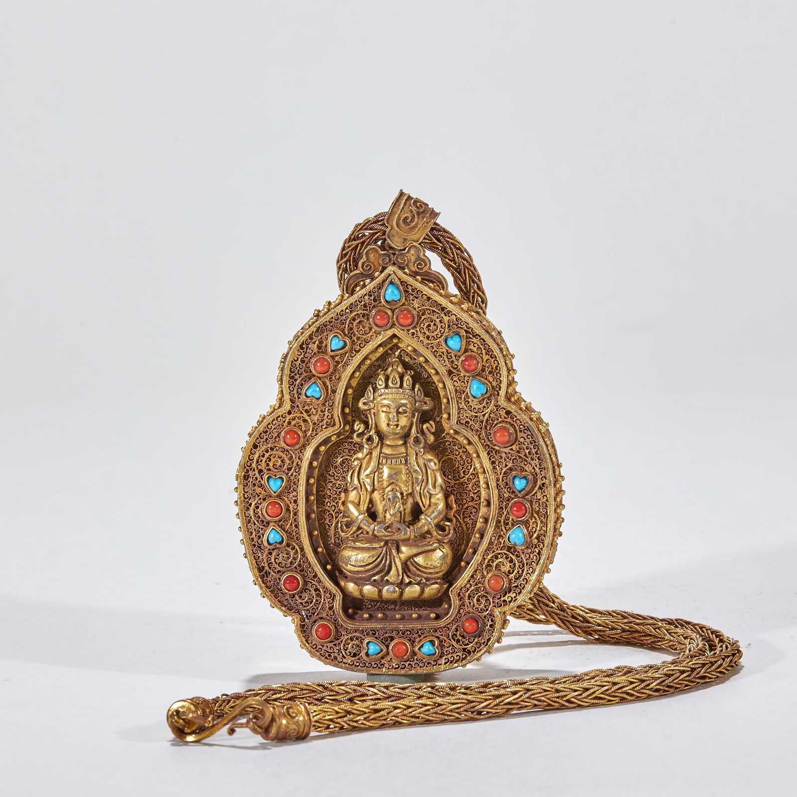 Gilt Silver Gem-Inlaid Gau Box: A gilt-silver inlaid gau box, a Tibetan Buddhist protective amulet box: the body is gilded and set with gems, coral and other stones, the face decorated with Buddhist motifs; inside it once held a