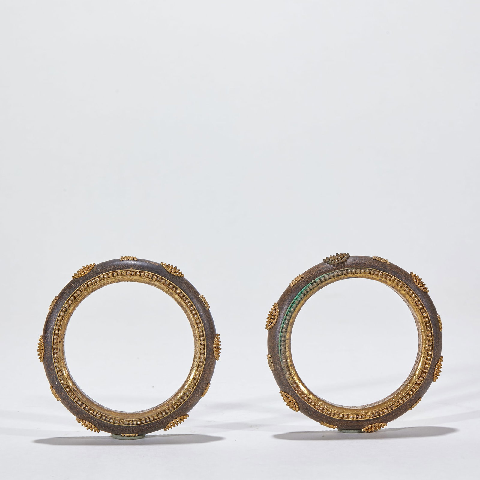 Pair of Agarwood Fu-Shou Inlaid Bangles: A pair of agarwood bangles, oily with a subtle fragrance. The surfaces are inlaid with fu-shou (fortune-longevity) motifs accented in gold or silver, meaning 'both fortune and long life'. Preserved