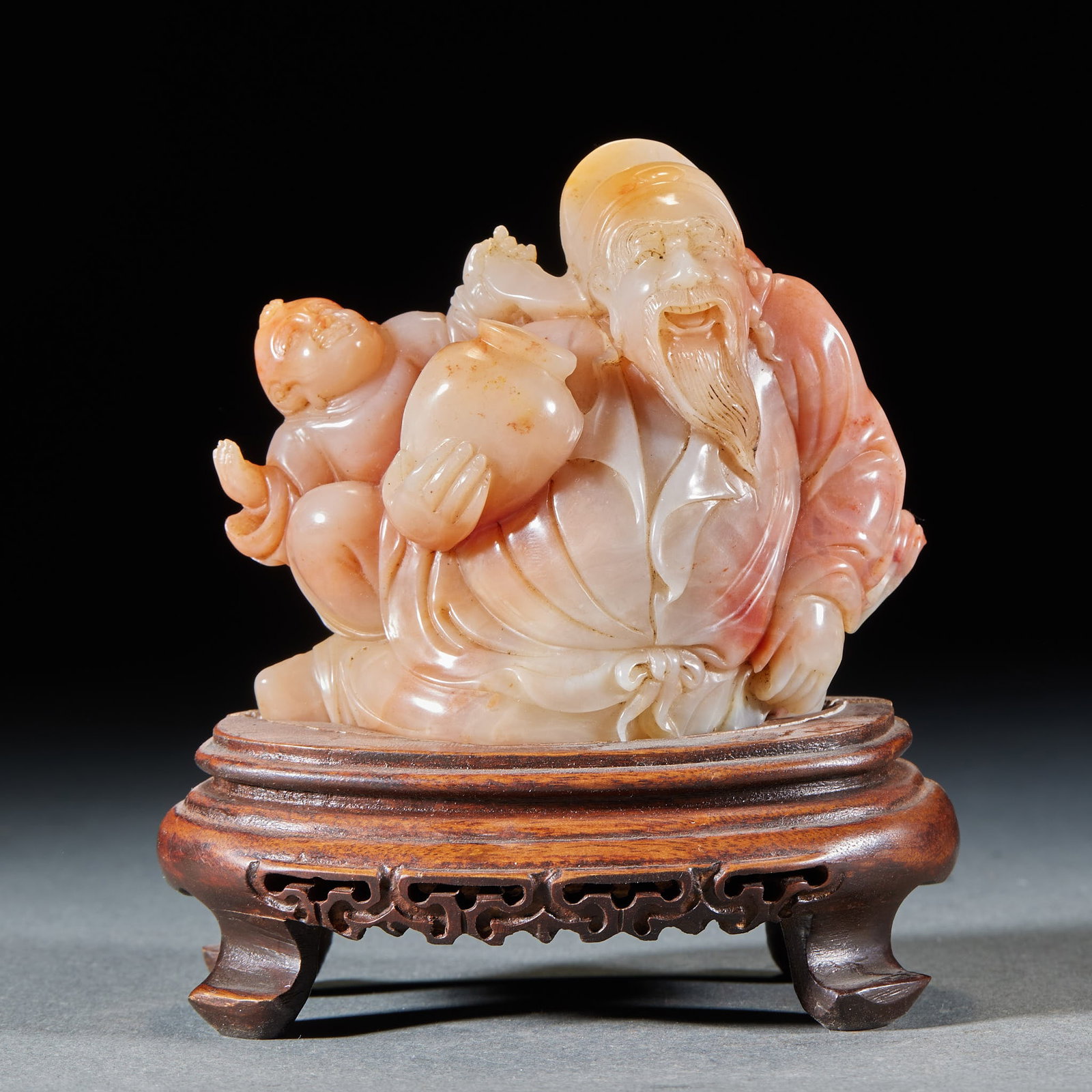 Shoushan Furong Stone Figure Ornament: A Furong stone round carving of a figure, immortal or lady, serene of face with flowing robes. The Furong stone is warm, red-and-white in tone, finely carved ?? a scholar's desk display. Net H 8 cm,