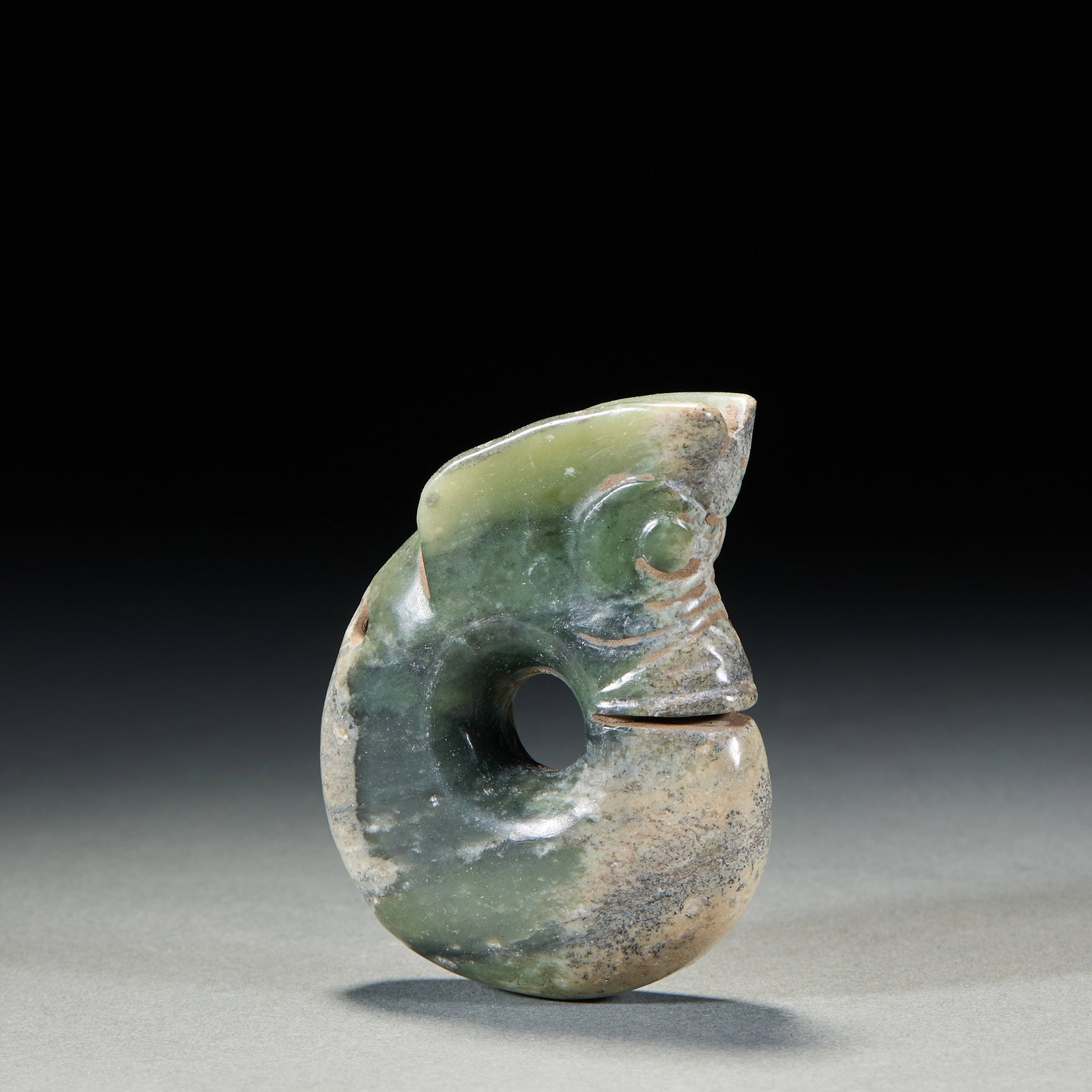 Jade Pig-Dragon: A jade pig-dragon in a coiled ring with head and tail joined; the large head is incised with eyes and ears, body curled. The jade is warm and calcified. A Hongshan-culture pig-dragon, vigorous and arc