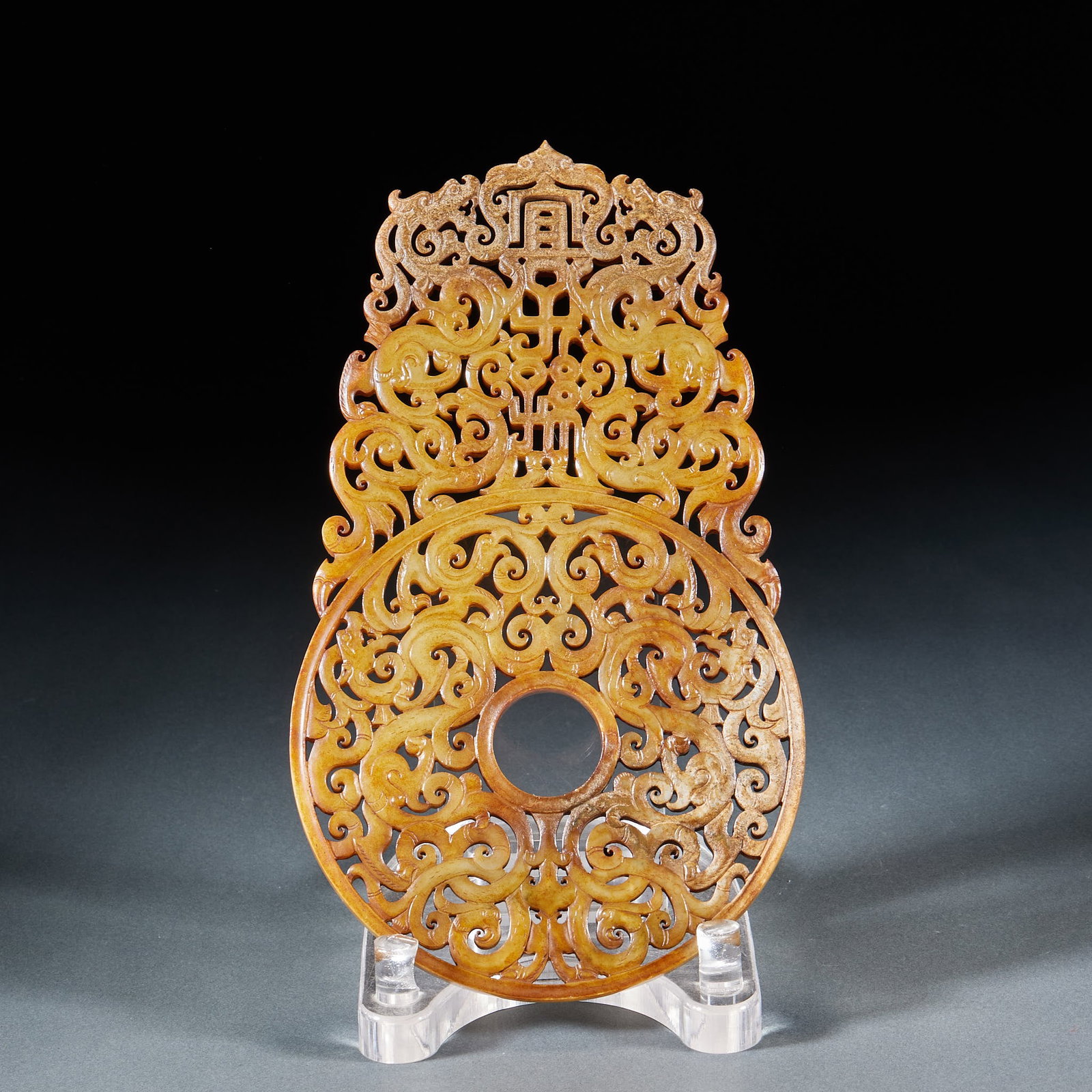 Pre-Ming 'Yi Zi Sun' (May Posterity Prosper) Jade Bi: A jade bi, round and flat, the face pierced or carved with the characters 'Yi zi sun' (may posterity prosper), symbolising flourishing descendants. The jade is warm and calcified, regularly carved ?? 