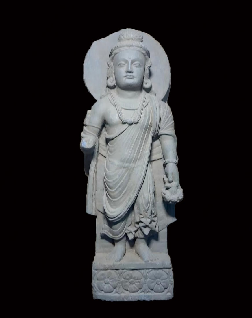 Stone Gandhara Standing Figure with Halo: A Gandhara stone standing figure: the Buddha stands upright with a boat-shaped halo behind, the face bearing Gandhara traits, robes heavy. Grey stone, solemnly carved ?? an early image from