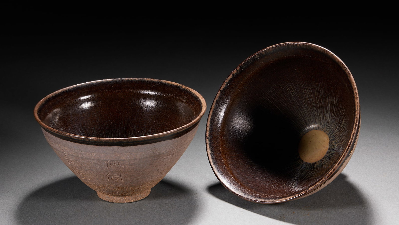 Pair of Inscribed Jian Ware Cups: A pair of Jian ware cups glazed black with hare's-fur or oil-spot patterns, the walls incised with characters, clearly. Song Jian-kiln-style tea cups, preserved as a pair ?? fine tea implements. H