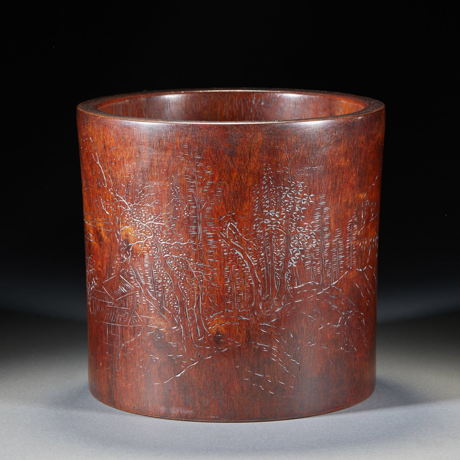 Huanghuali 'Landscape and Dwelling' Brush Pot: A Huanghuali brush pot with the exterior carved in relief with a landscape scene of distant mountains, near water and hidden houses, finely cut. The wood has magnificent grain ?? a scholar's display