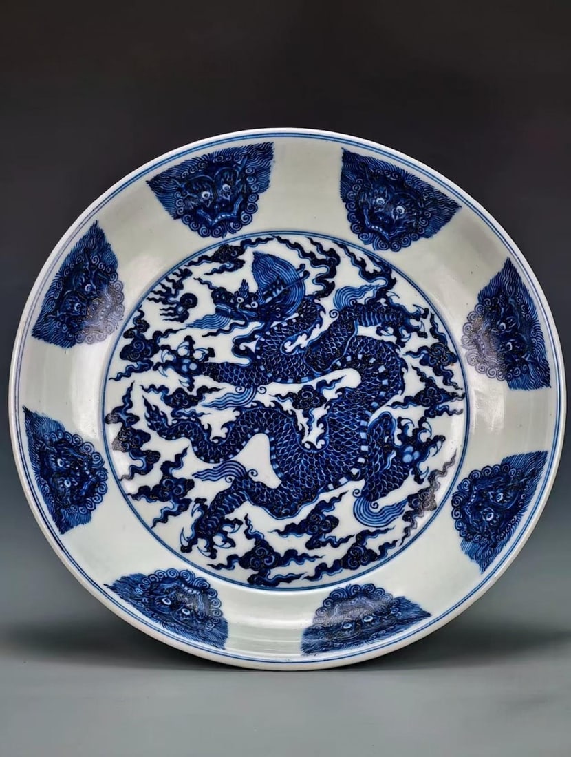 Underglaze-Blue Beast-Mask Cloud-Dragon Display Dish: A display dish painted in the centre with a fierce cloud-dragon, the exterior with beast-mask motifs. Rich blue and lustrous glaze ?? a display dish. H 6.8 cm, Diameter 41 cm.