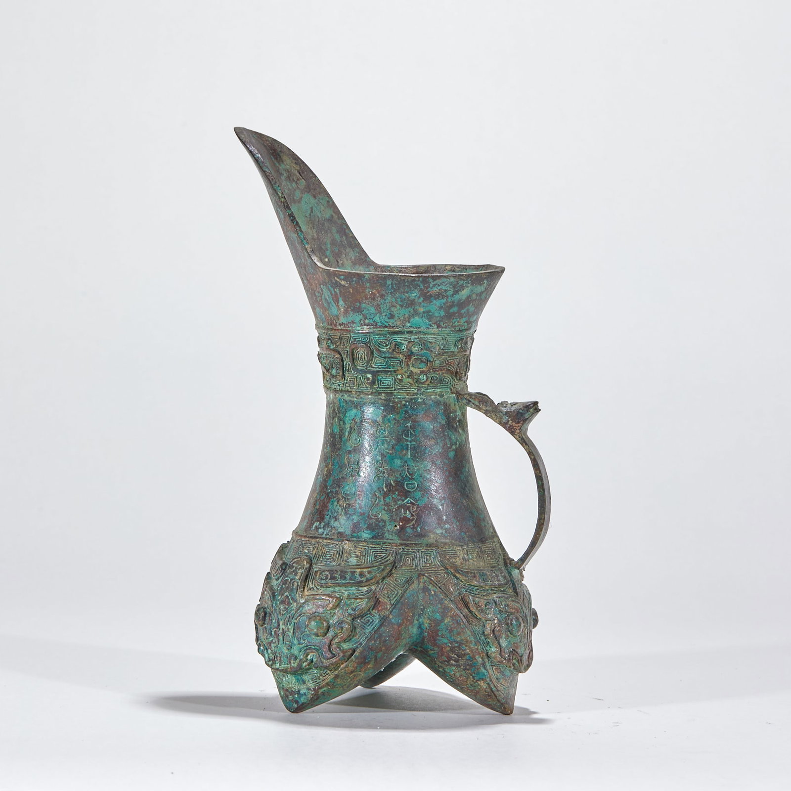 Pre-Ming Copper Tripod Jue Cup: A copper tripod jue, the ancient wine ritual cup, with round belly, three feet, and spout and tail at one side. Covered in green patina, dignified ?? a pre-Ming bronze jue. H 23 cm, L 11 cm, W 11 cm,