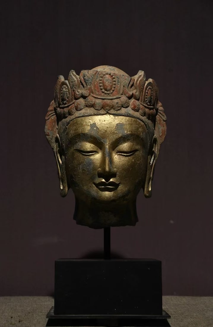 Gold-Foil Bodhisattva Head: A wood or stone Buddha head surfaced with gold foil, solemn and kindly. The gold is warm and the image fine ?? a Buddhist image fragment or offering. H 25 cm.